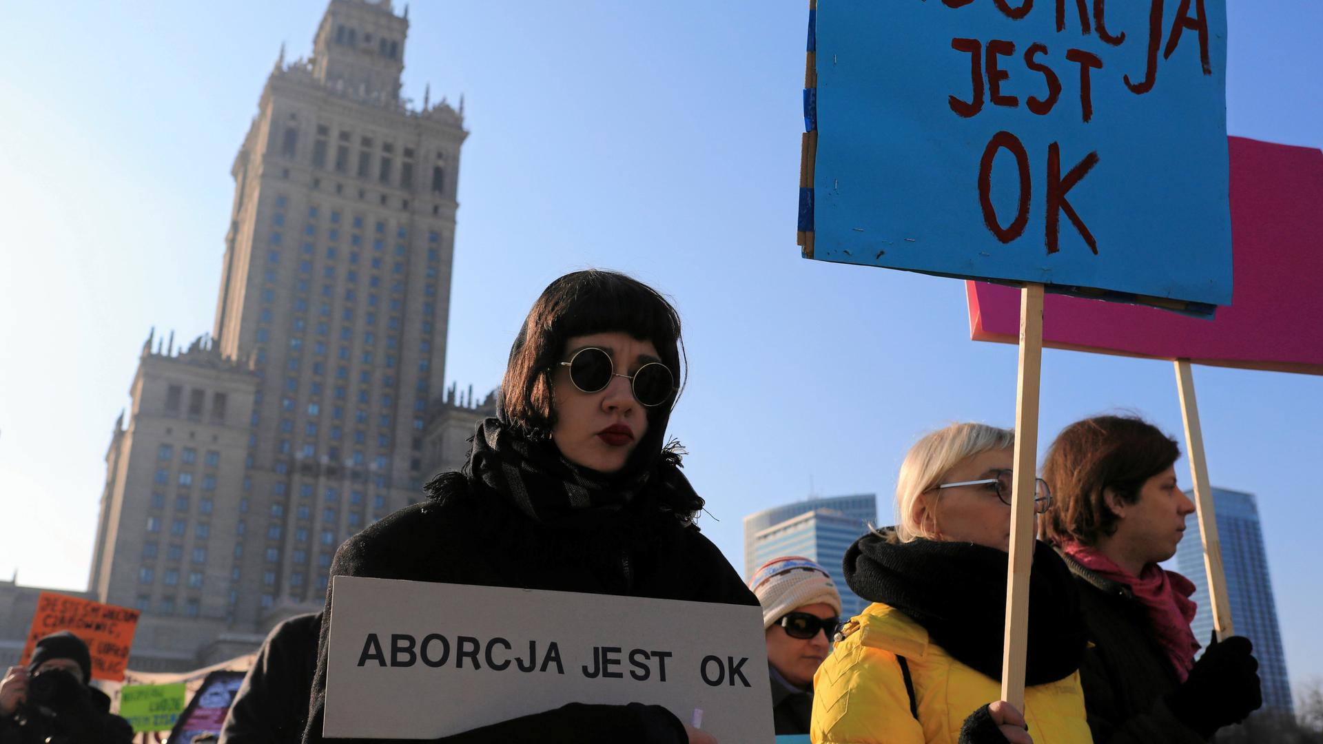 woman wearing sunglasses holds sign that says "abortion is ok"