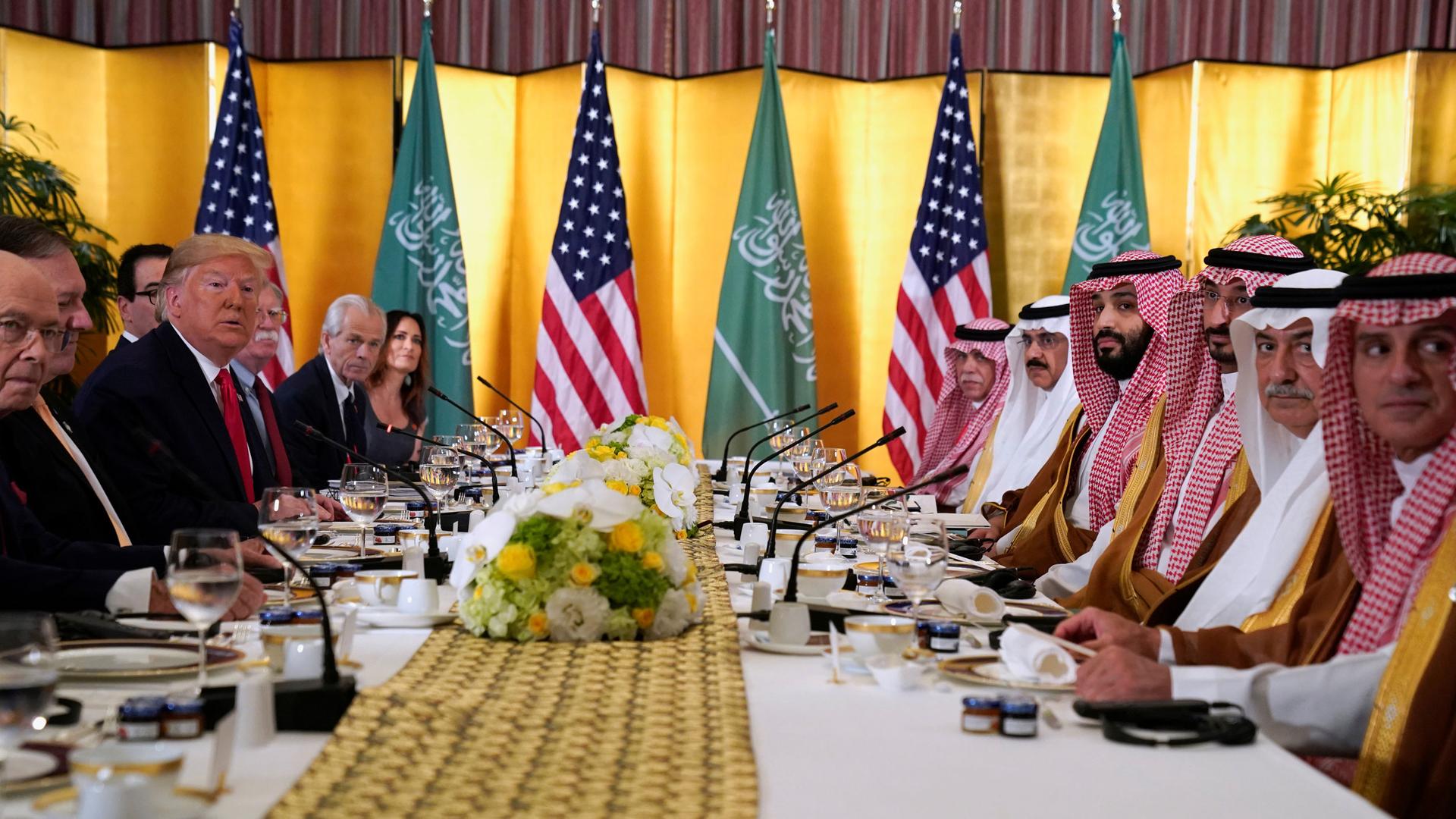 A long table is shown from one end with President Trump's dark-suit-clad team sits across from Saudi Arabia's Crown Prince Mohammed bin Salman's team wearing traditional checkered head dresses.