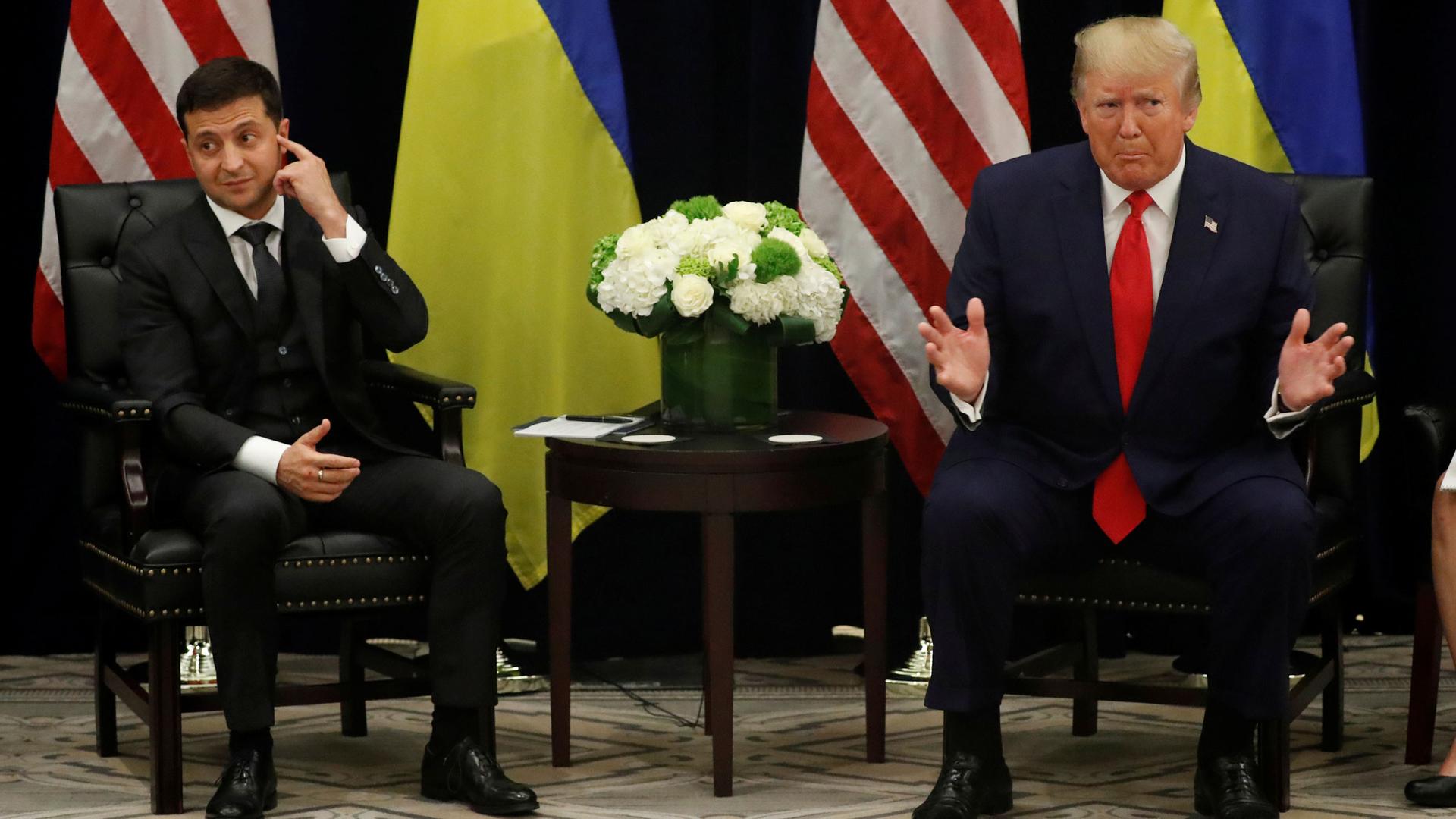 Ukraine's President Volodymyr Zelenskiy is shown seated next to US President Donald Trump with their respective flags placed behind them.