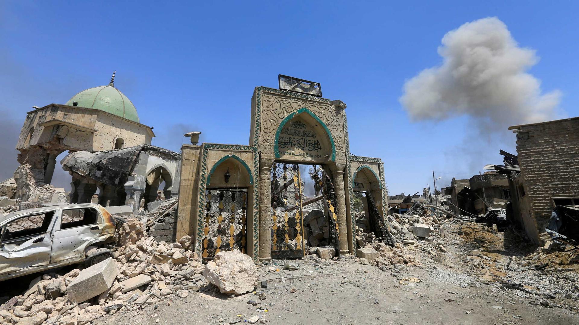 The front of mosque is seen amid rubble. Behind the door, is a distinctive blue dome.