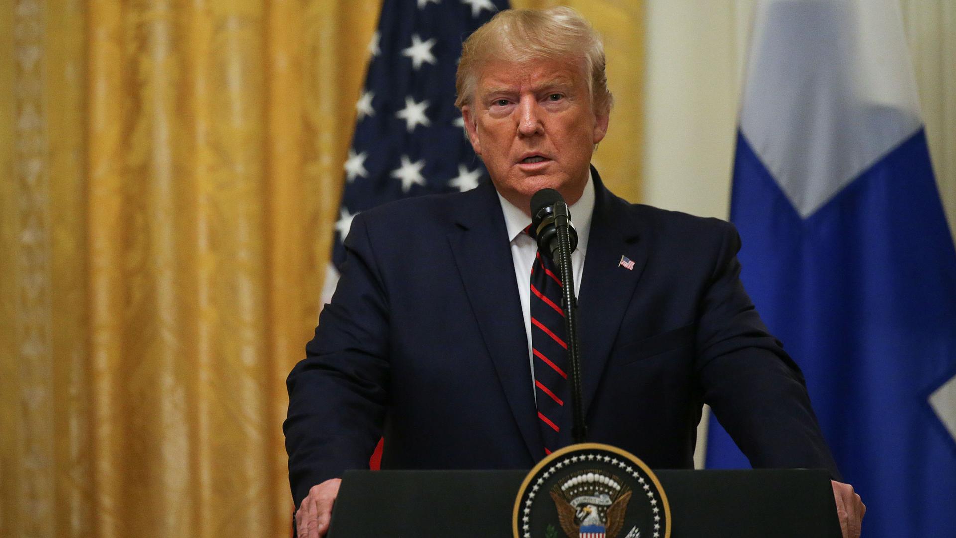 US President Donald Trump is shown standing at a podium with a seal for the US president.