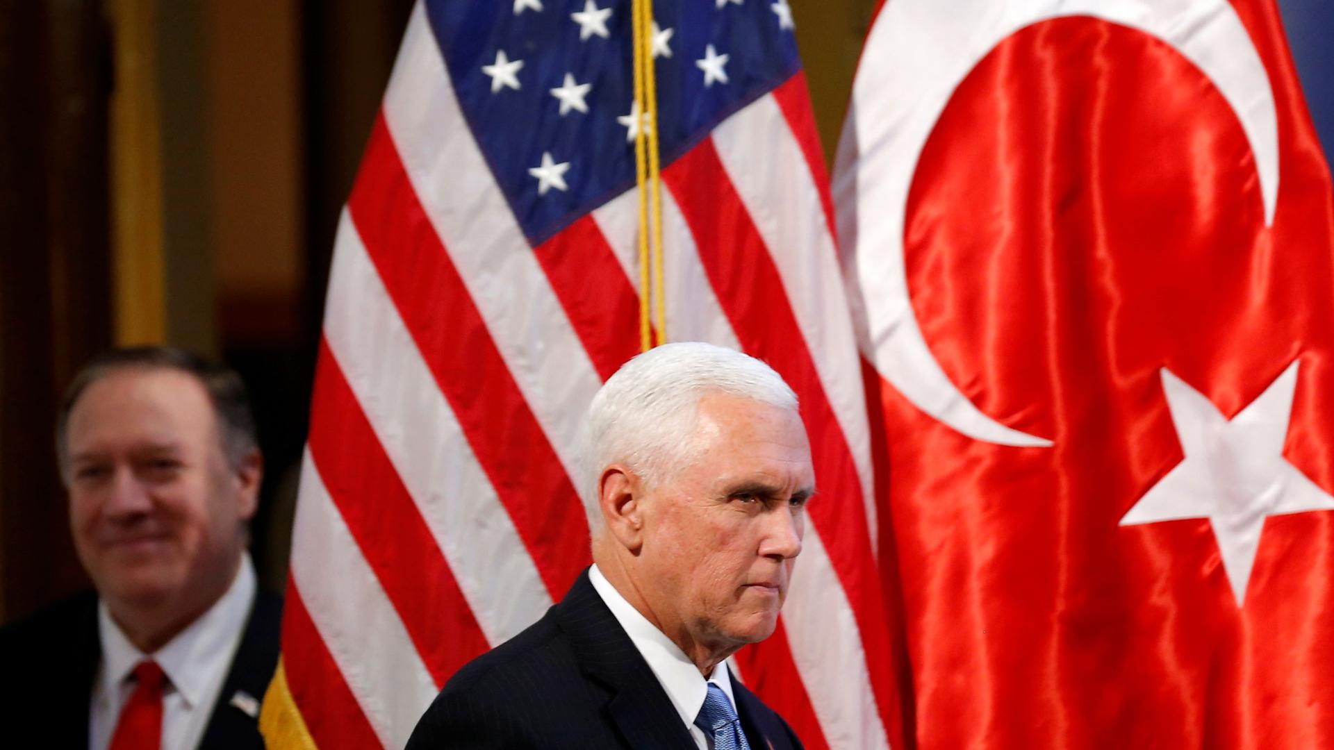 US Vice President Mike Pence is shown wearing a dark suit and blue tie and walking past the US and Turkey flags