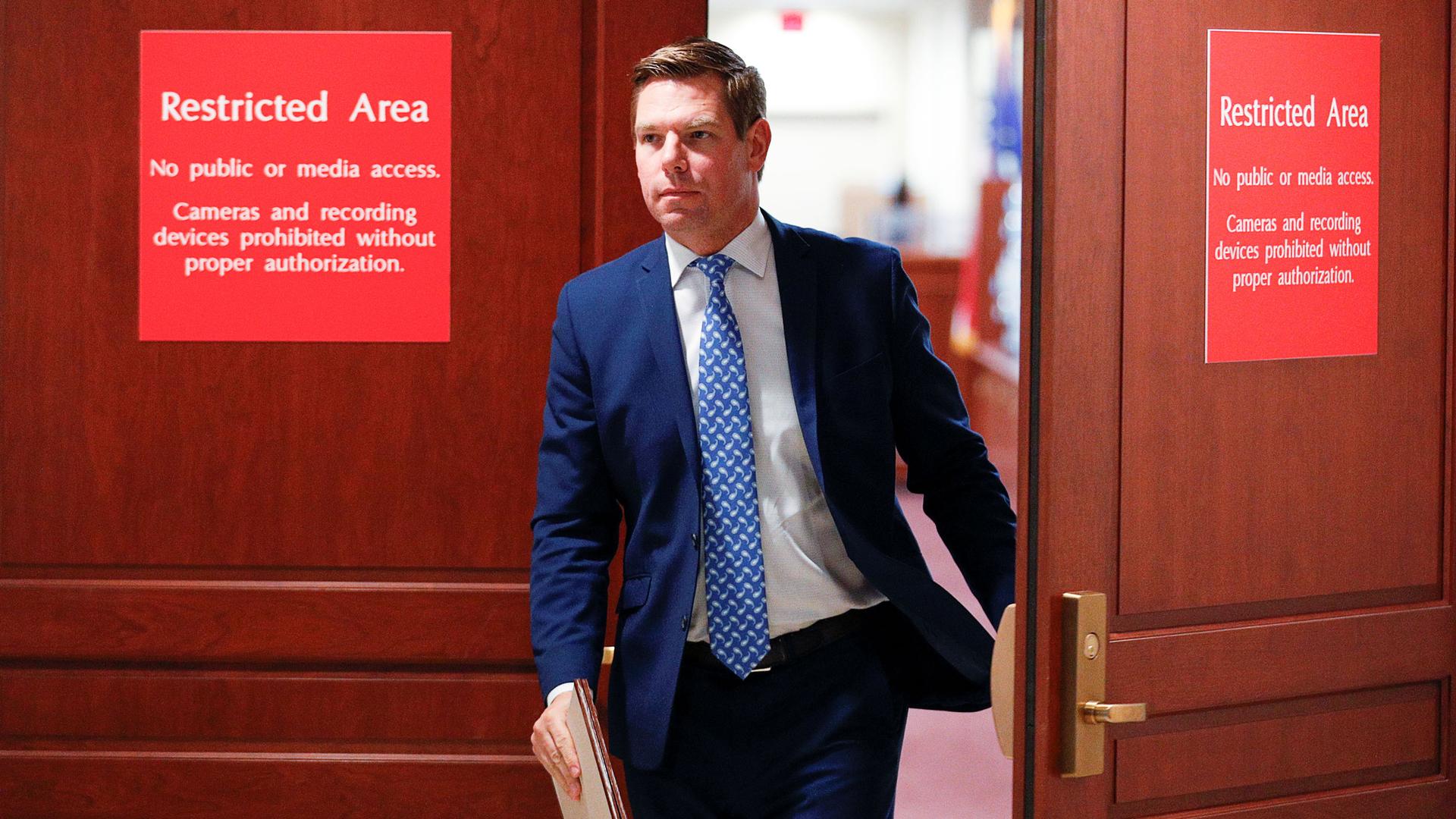 Representative Eric Swalwell is shown wearing a blue suit and exiting a room with red signs saying "Restricted Area."