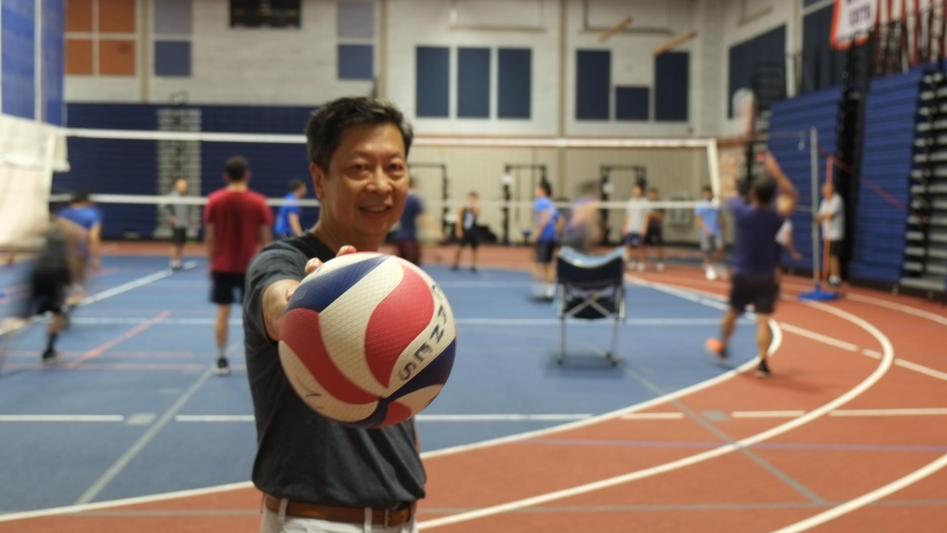 An Asian man holds a volleyball on the court