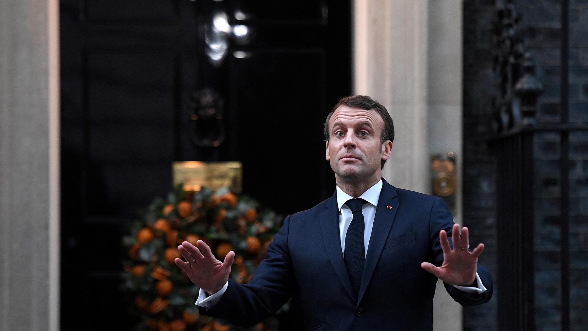 France's President Emmanuel Macron is shown with both of his hands outstretched and wearing a blue suit.