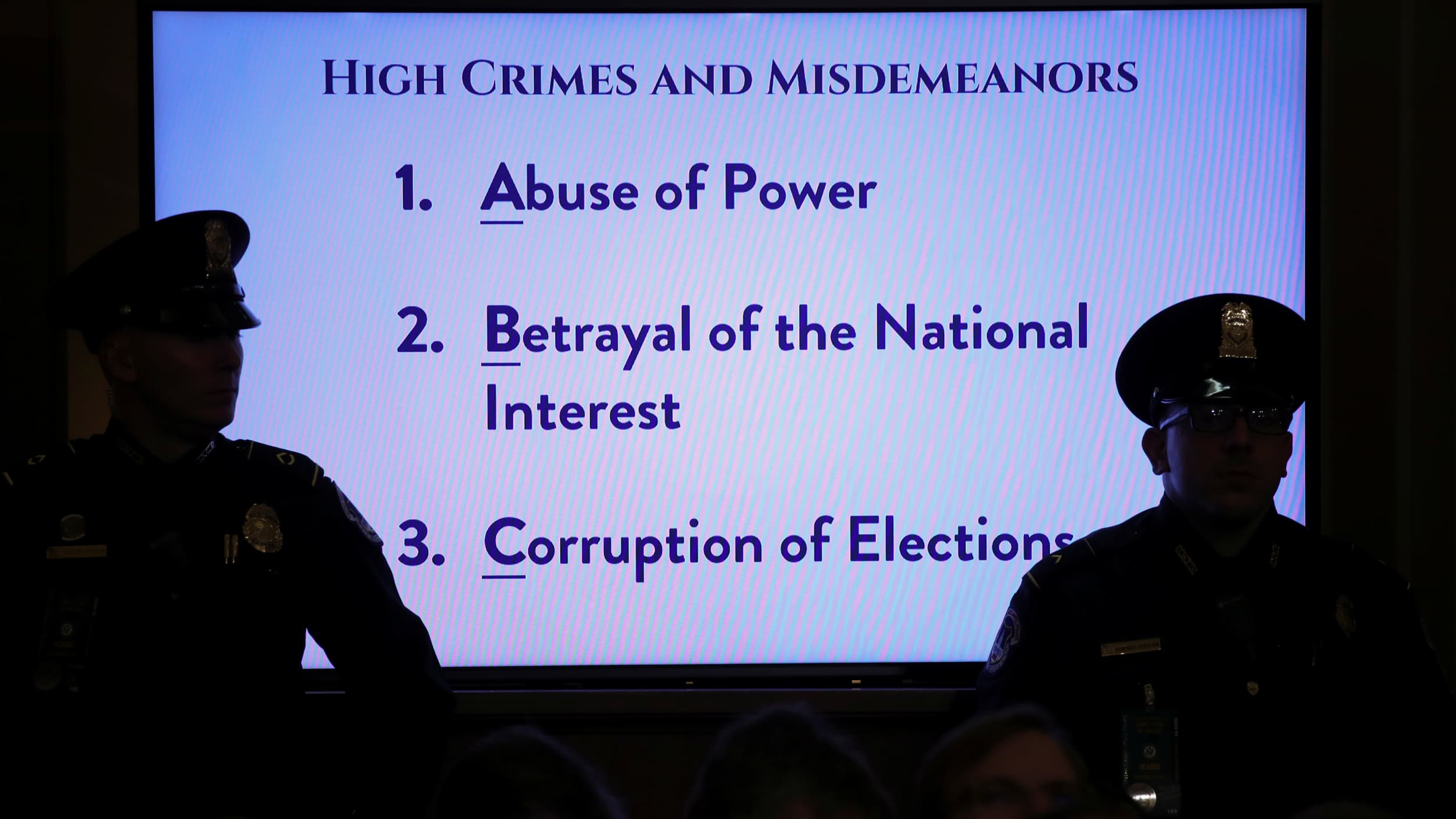 US Capitol police officers are shown in shadow standing in front of a brightly lit TV monitor displaying several sentences of text related to US President Donald Trump's alleged impeachable offenses.