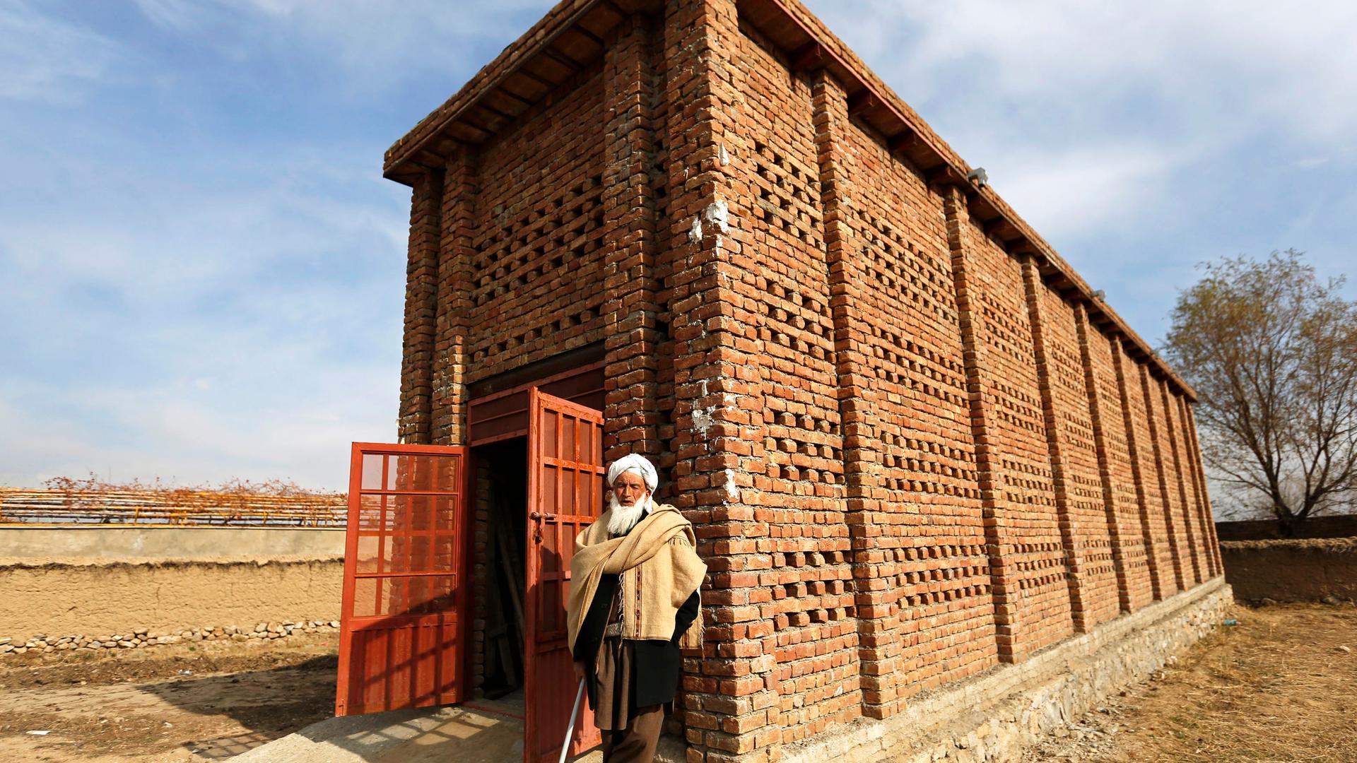 A man stands in front of a brick building in rural setting