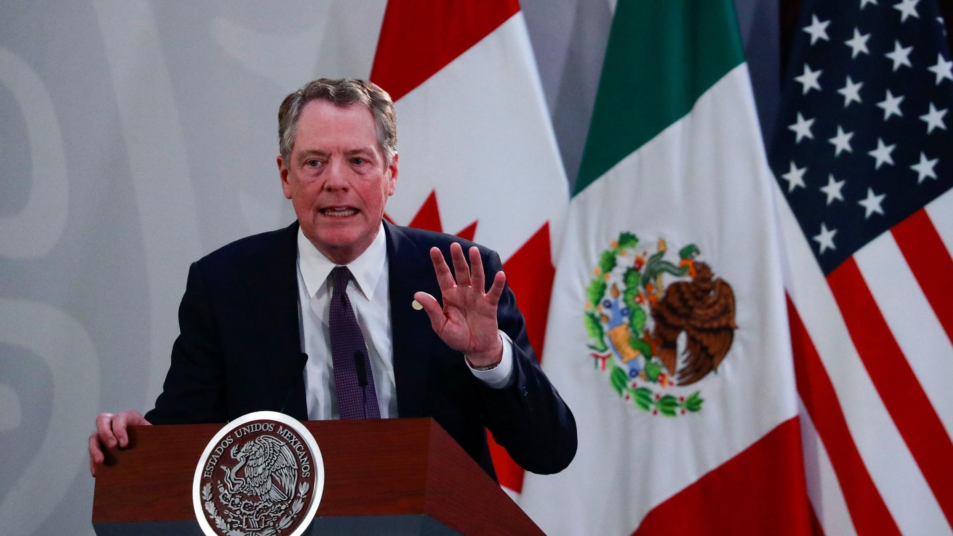 US Trade Representative Robert Lighthizer is shown speaking from a podium with the US, Mexico and Canadian flags behind him.