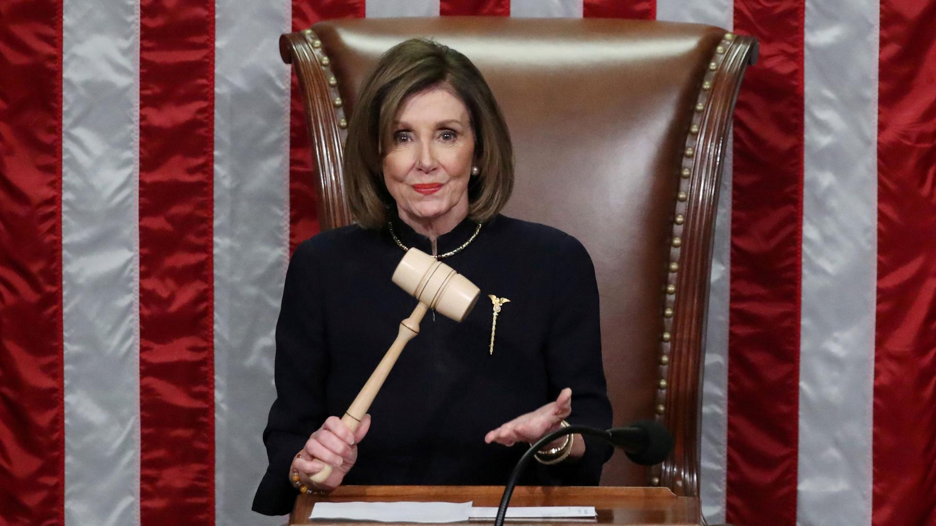 US Speaker of the House Nancy Pelosi wields the gavel and stands in front of a large US flag.