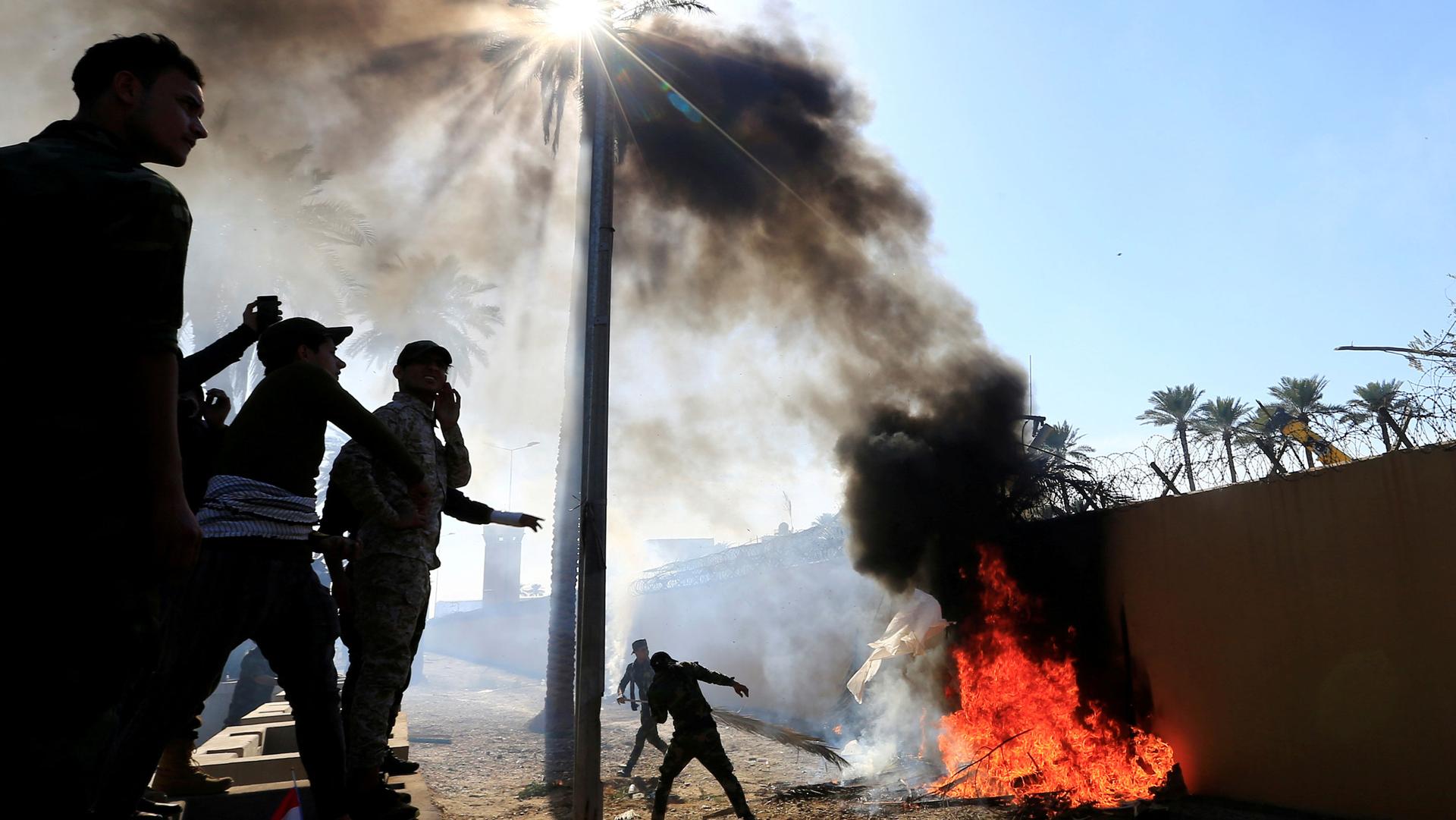 The US Embassy wall is shown set on fire by a group of people adjacent.