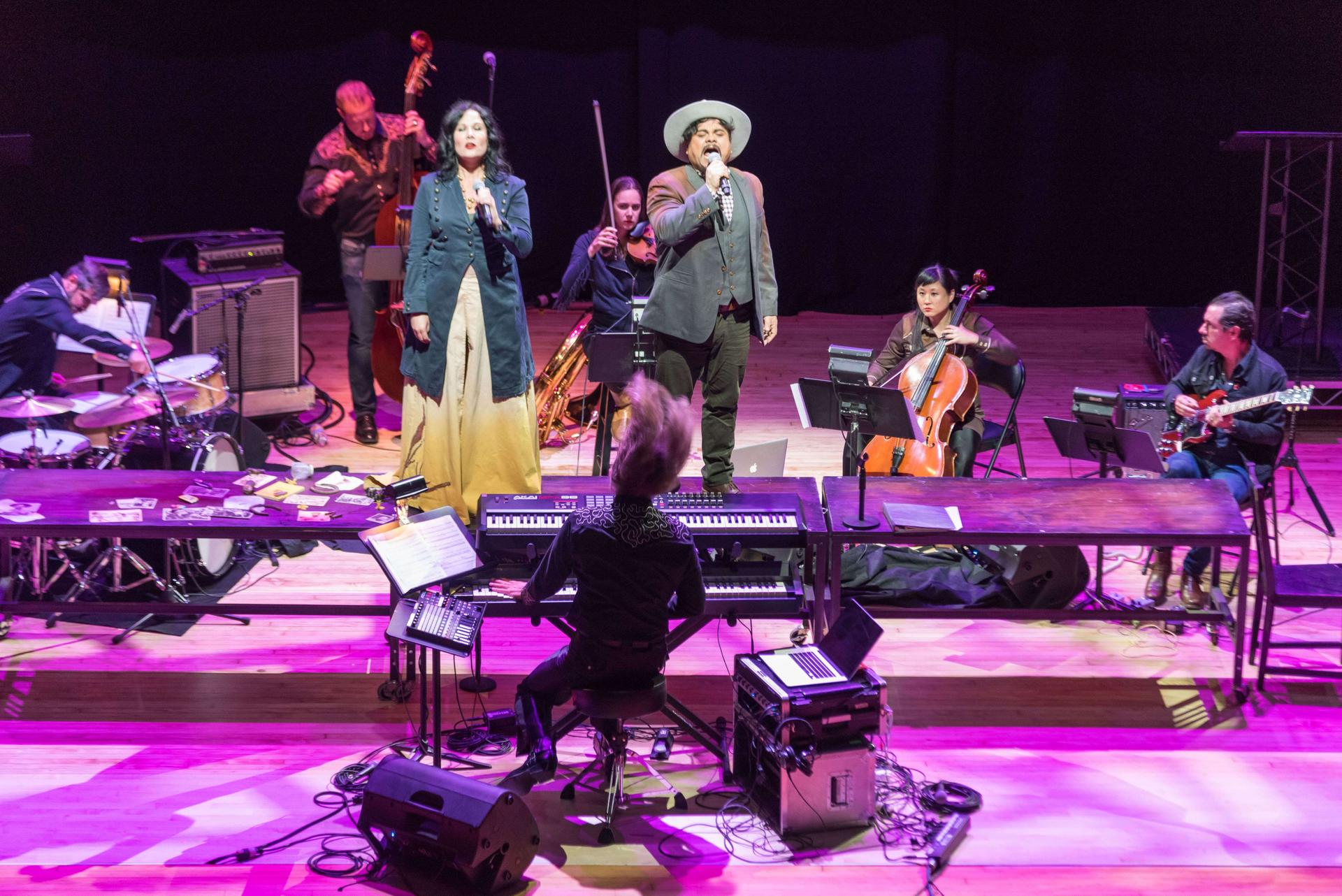 a full band on stage, singing and performing in the glow of purple stage lights