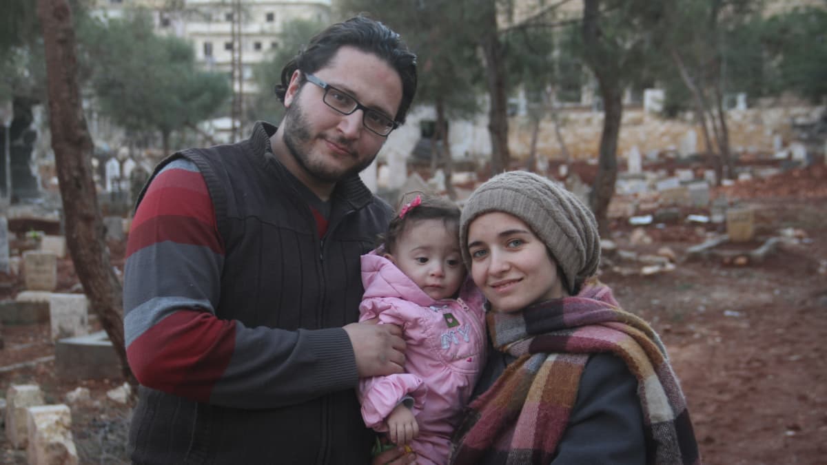 Mother, father and baby pose outside for a photo in wooded area