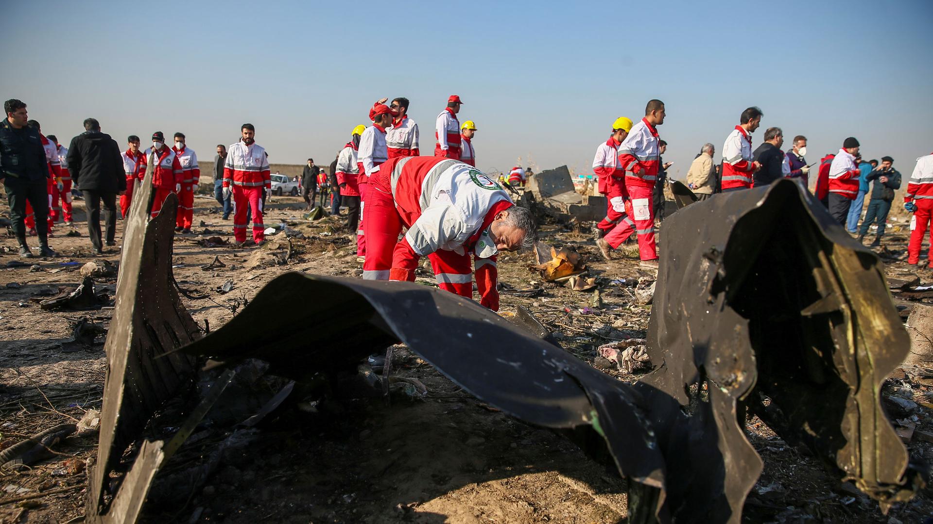 Dozens of workers dressed in red and white overalls are shown at an airplane crash site.