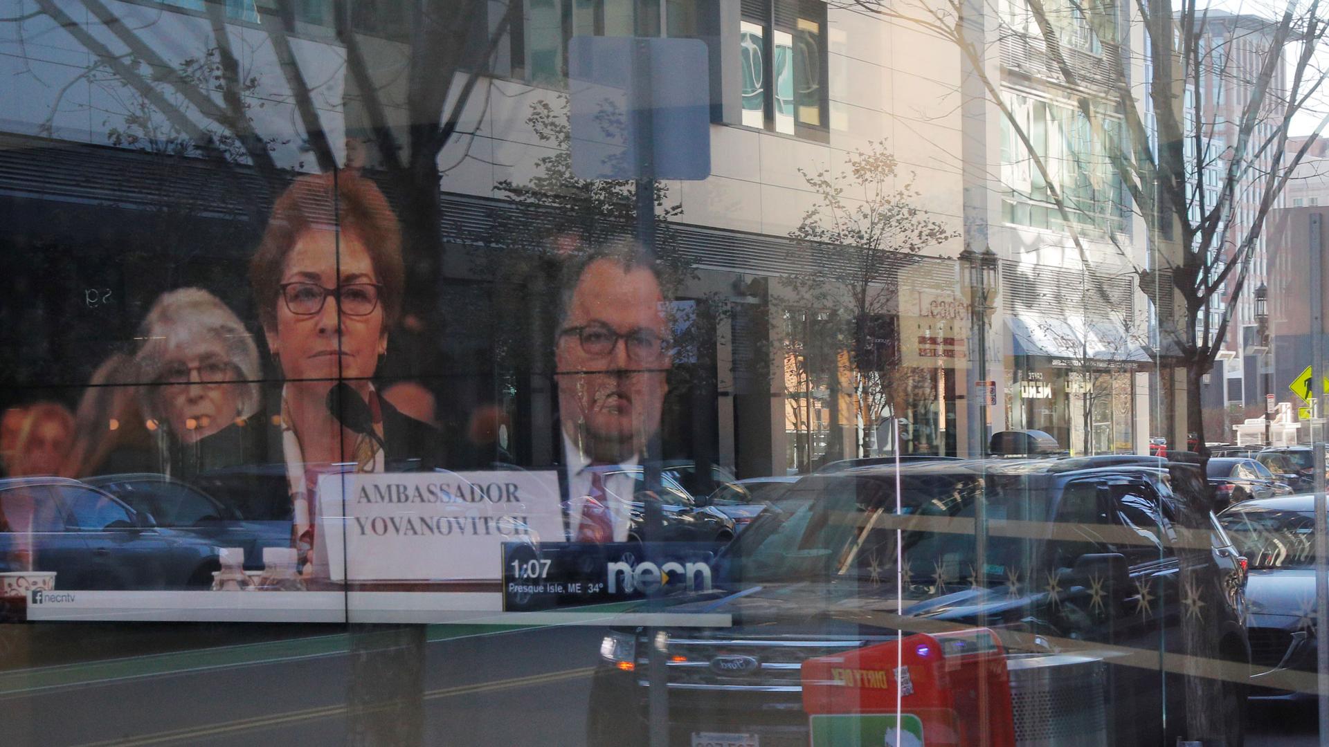 A television with former US Ambassador to Ukraine Marie Yovanovitch on screen is shown through a wall of glass.