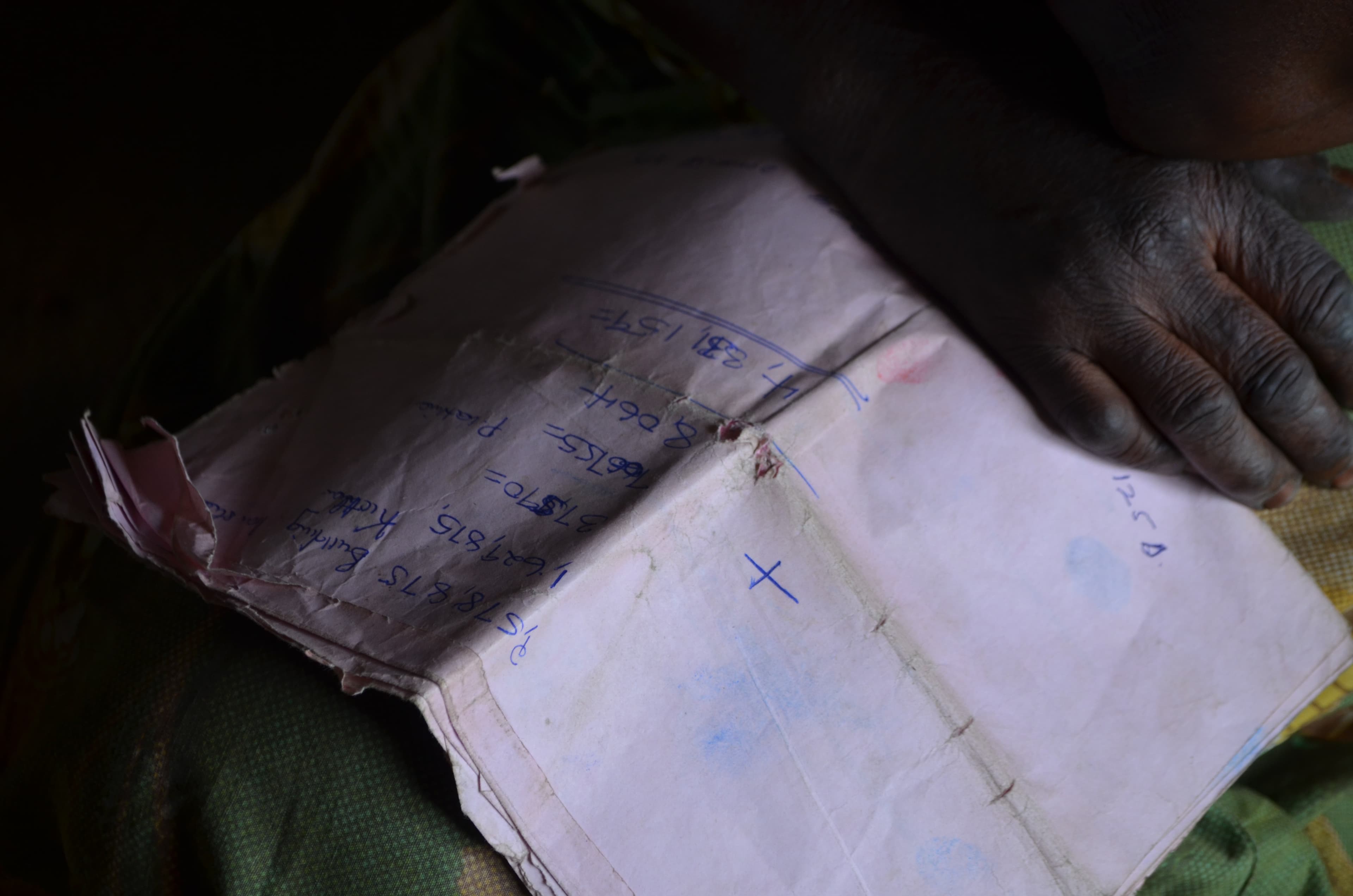 A hand holds a piece of paper with numbers written on it with pen ink