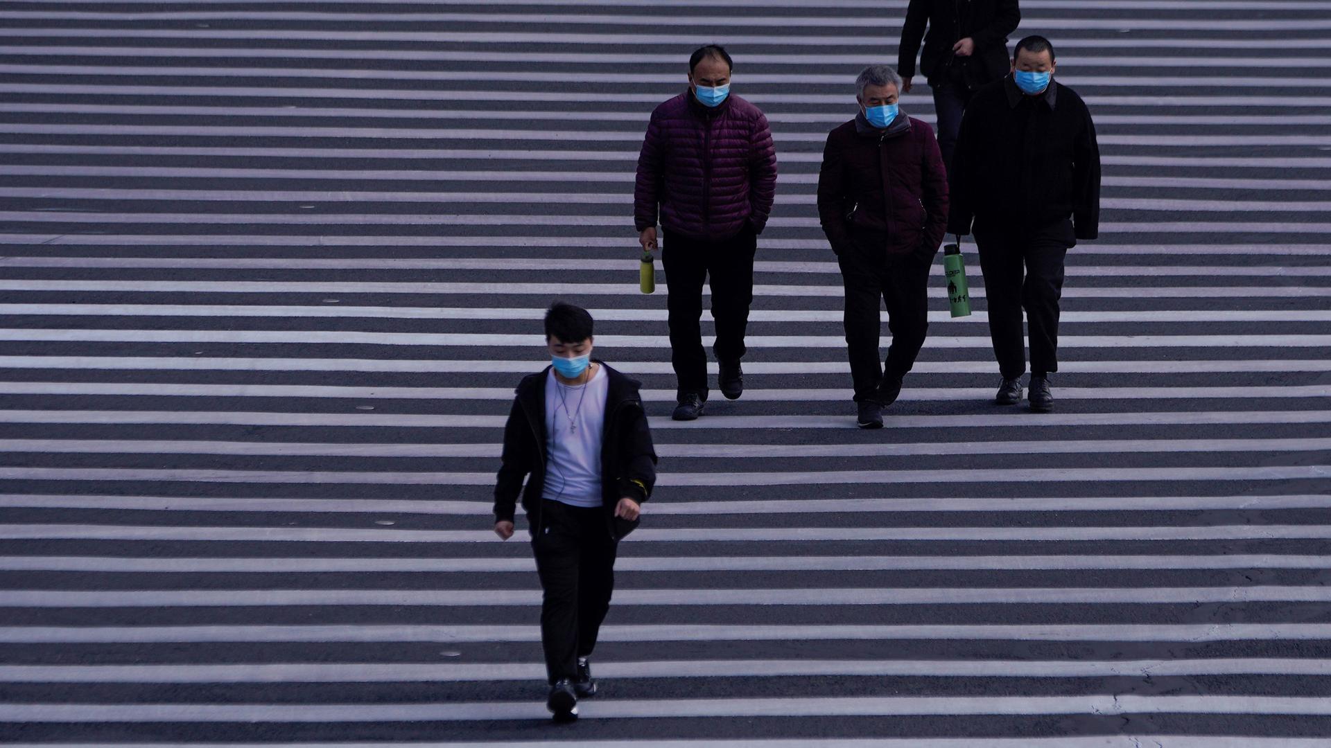 Several people are shown walking on a white-lined road and wearing face masks.