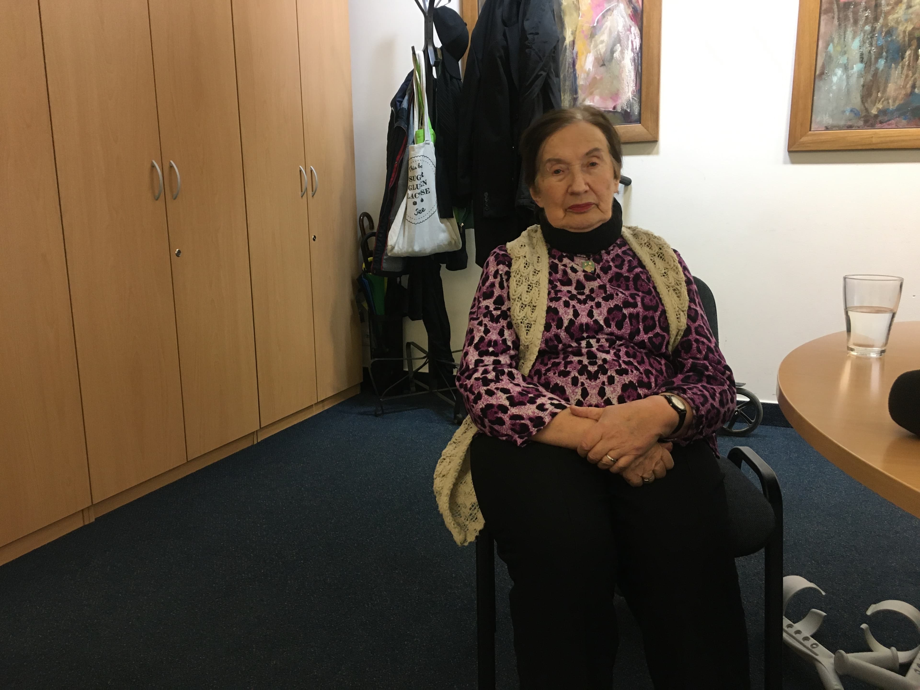 Zofia Radzikowska, 84, wears a purple shirt and sits with her hands crossed.