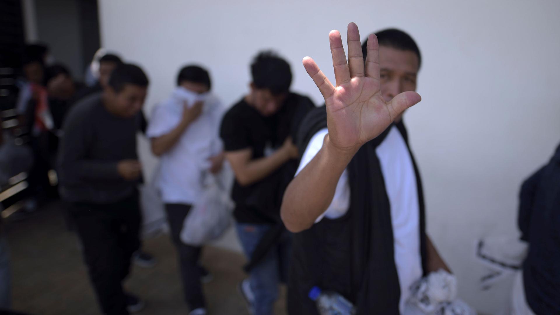 A man is show holding his hand up to the camera as he walks with several over people.