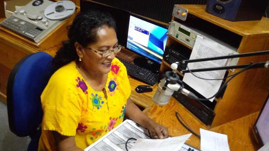 A woman wears a bright yellow blouse and sits in a radio studio