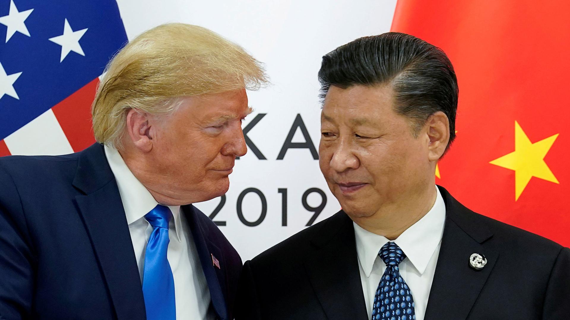 US President Donald Trump and China's President Xi Jinping are shown both wearing dark suits and ties while standing in front of the US and Chinese flags.