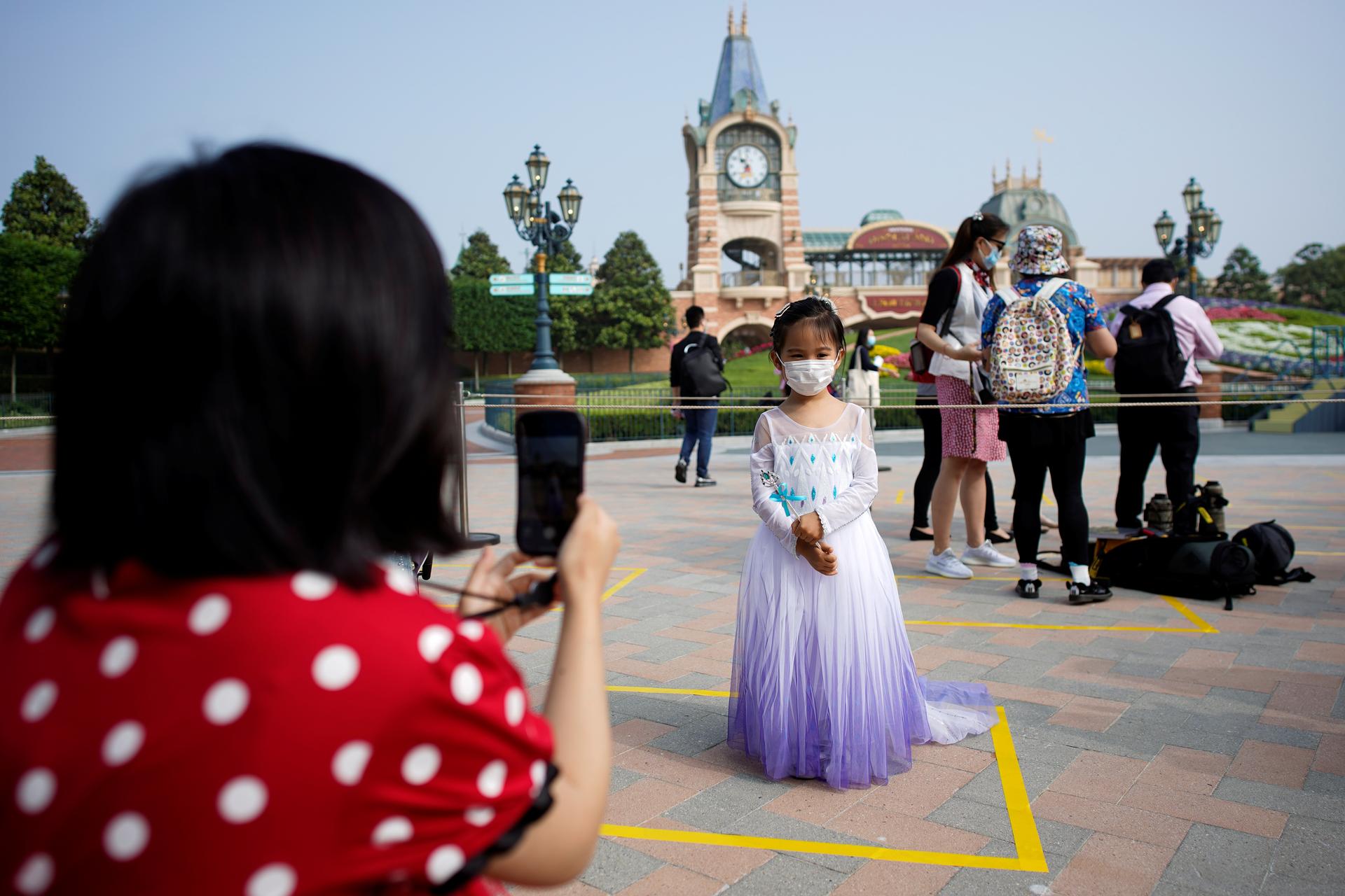 A mother photographs her child wearing a face mask and a princess gown at Disneyland in Shanghai.