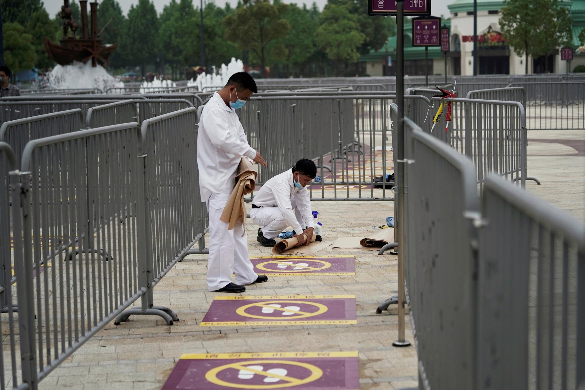 Workers wearing face masks paint social distance markers on the ground at Shangahi Disneyland
