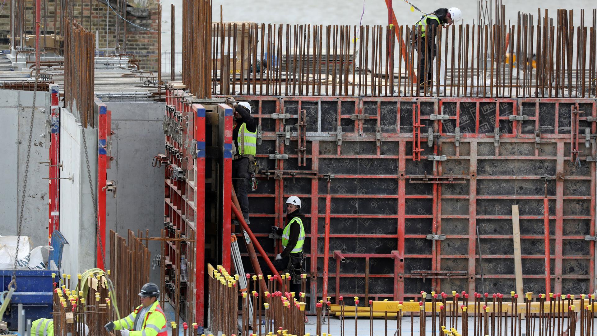 Several construction workers are show wearing hard hats and working on the framing of a building.