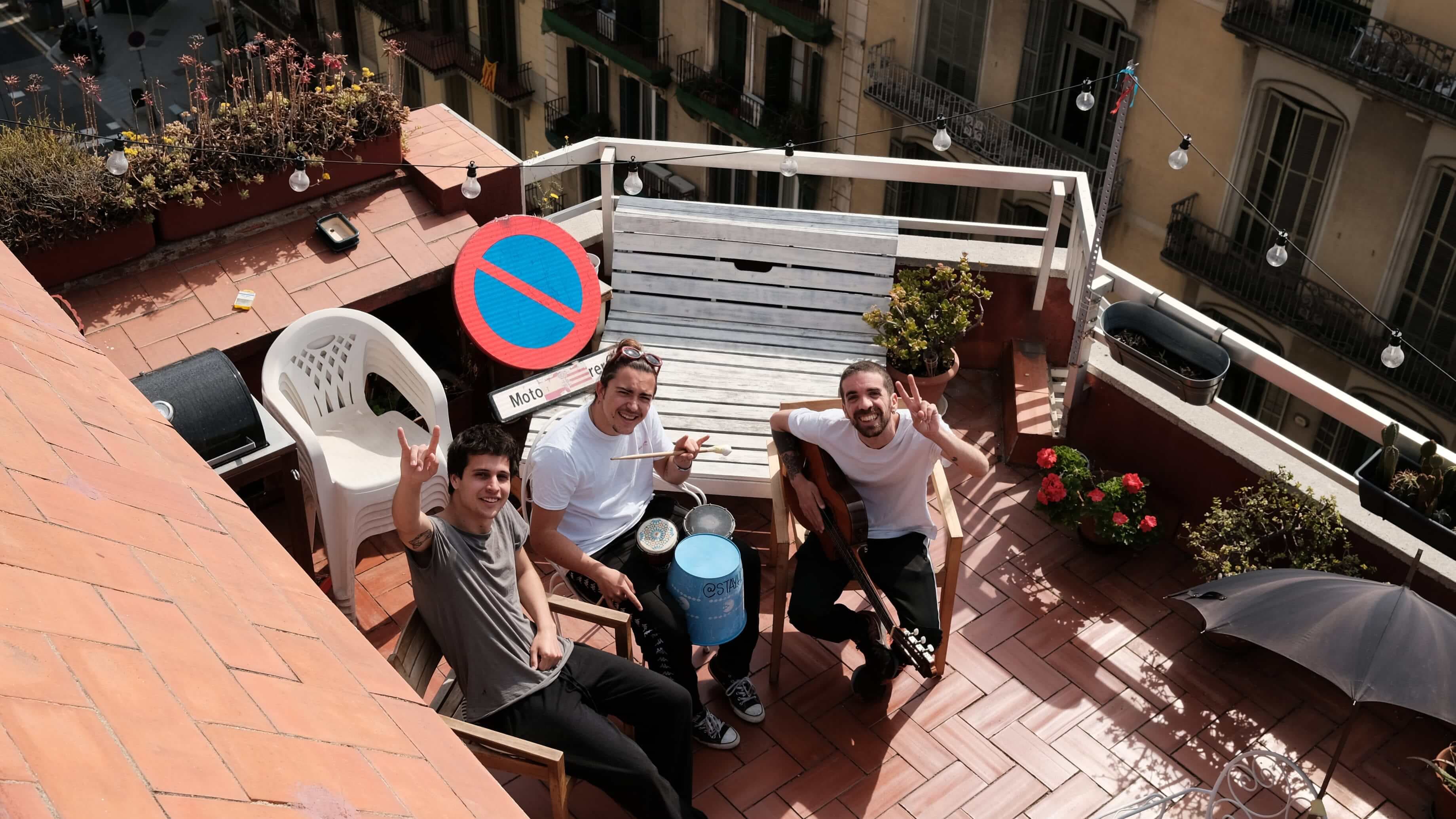 Three musician roommates sit on their rooftop and look up at the camera