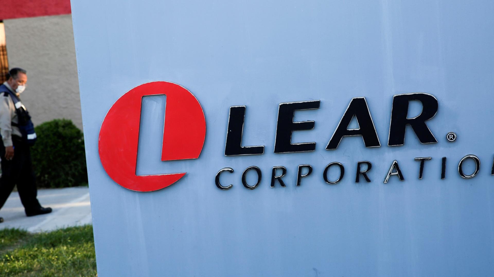 The logo of Lear Corporation, a Michigan-based car seat maker, near a man walking with a face mask