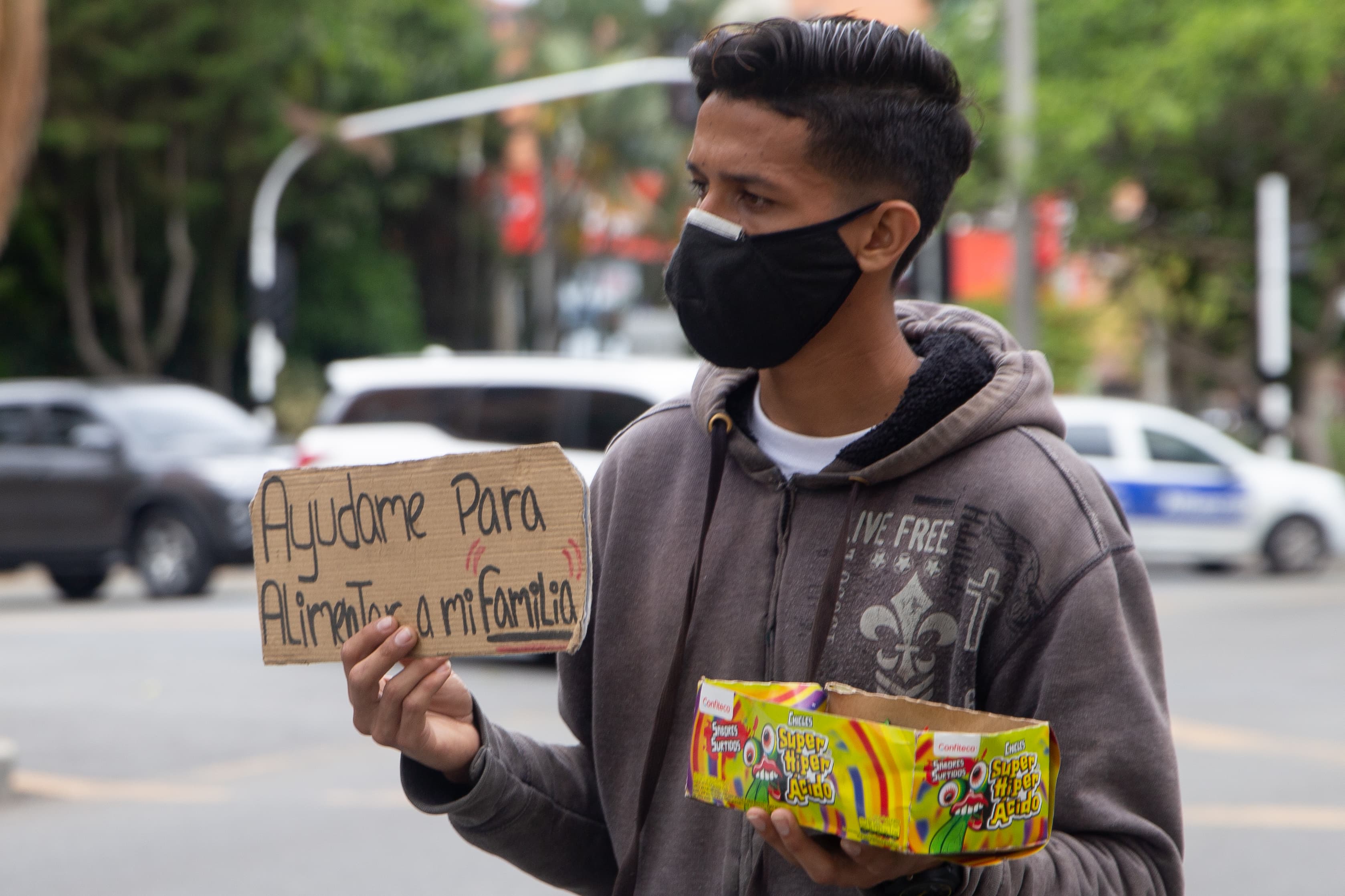 A young man wearing a black face mask sells colorful candies on the street.