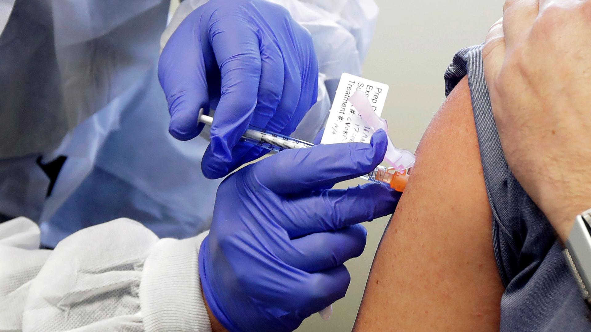 A close-up photograph shows a researcher hearing blue protective gloves and inserting a syringe into the shoulder of a subject.
