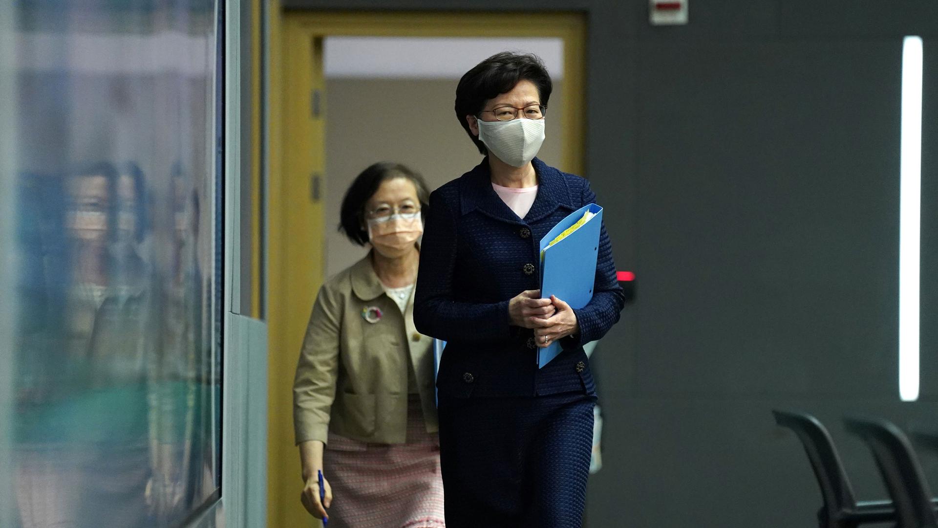 Hong Kong Chief Executive Carrie Lam is shown walking into a room and holding a blue folder.