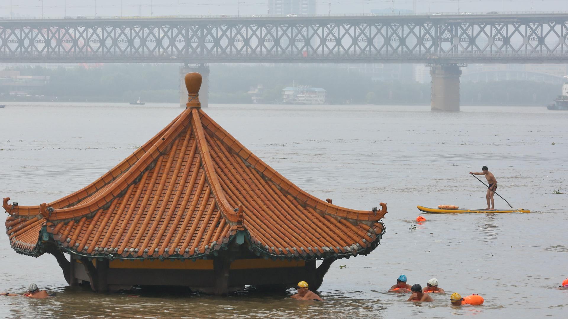 People swim near a partially flooded pavilion near banks of Yangtze River