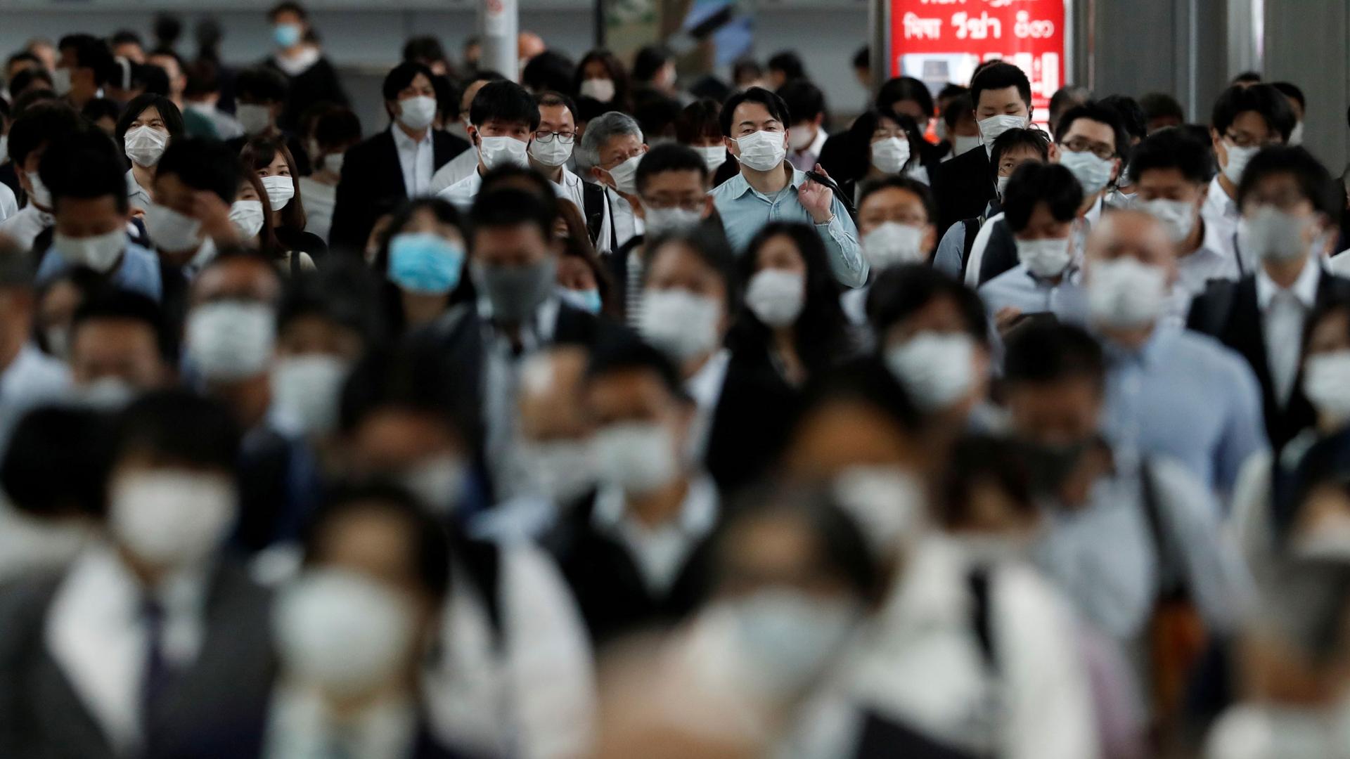 A large crowd of people are shown walking and wearing protective face masks in a train station.