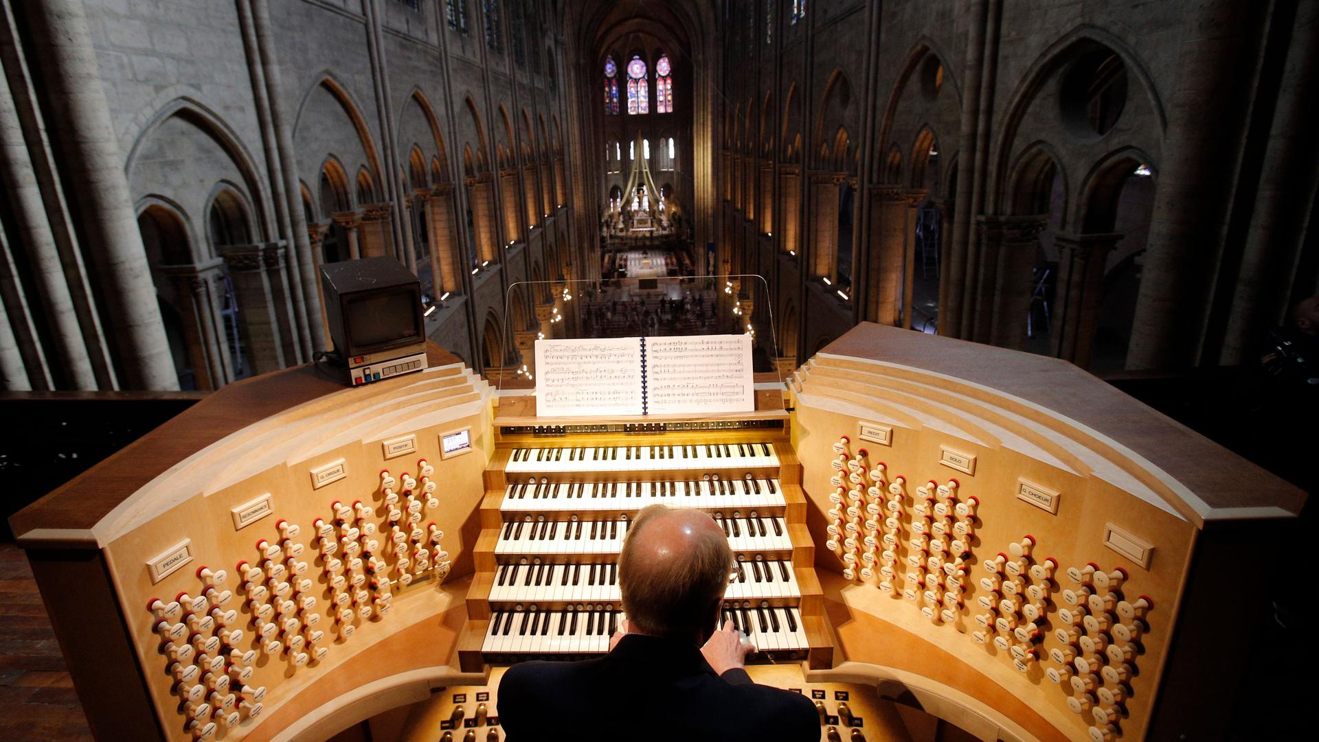 A man is shown from behind sitting at Notre Dame's organ with five rows of keys.