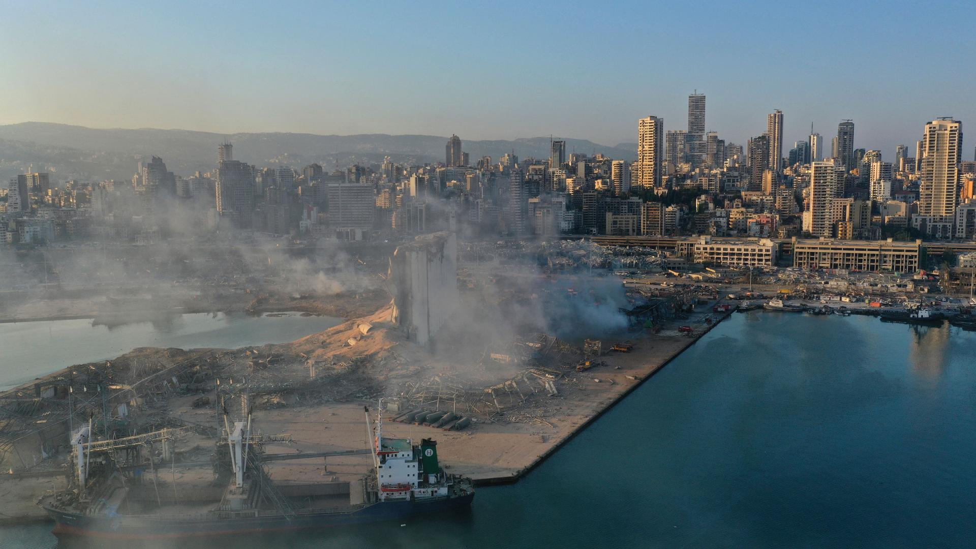 A view of Beirut's port is shown, flattened from an explosion and smoke rising from the rubble