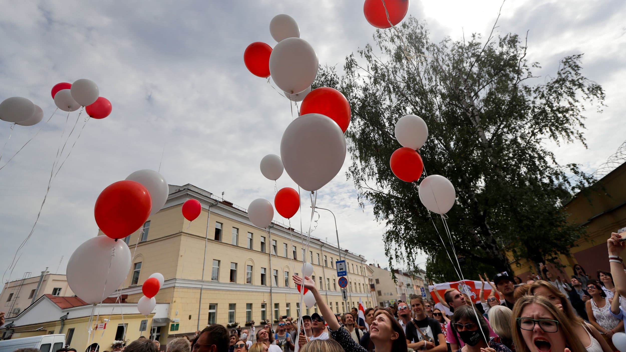 A large crowd of people are shown releasing red and white balloons into the air.