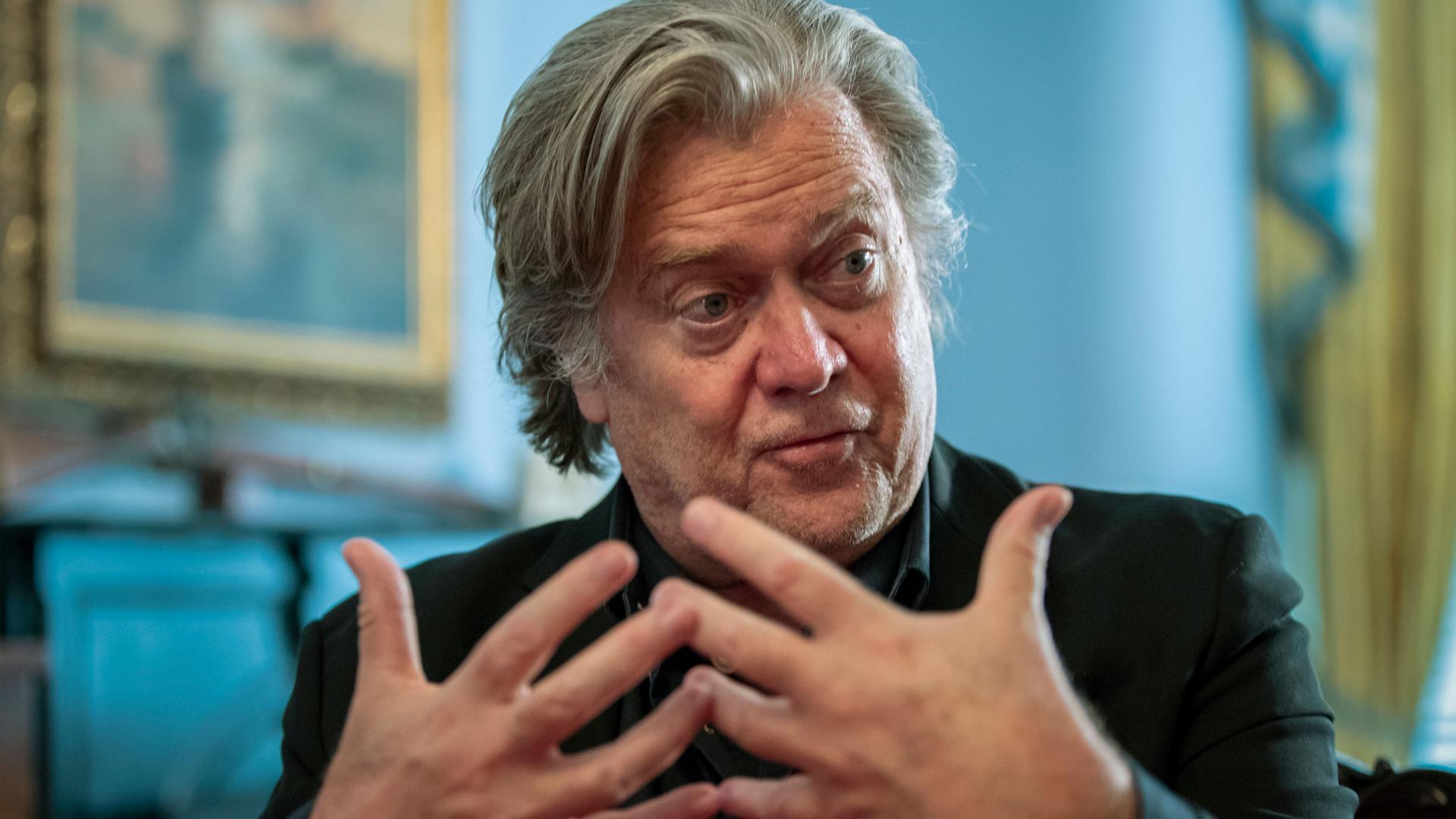 A close-up photograph of Steve Bannon who has his hands out in front in a gesture whiile speaking.