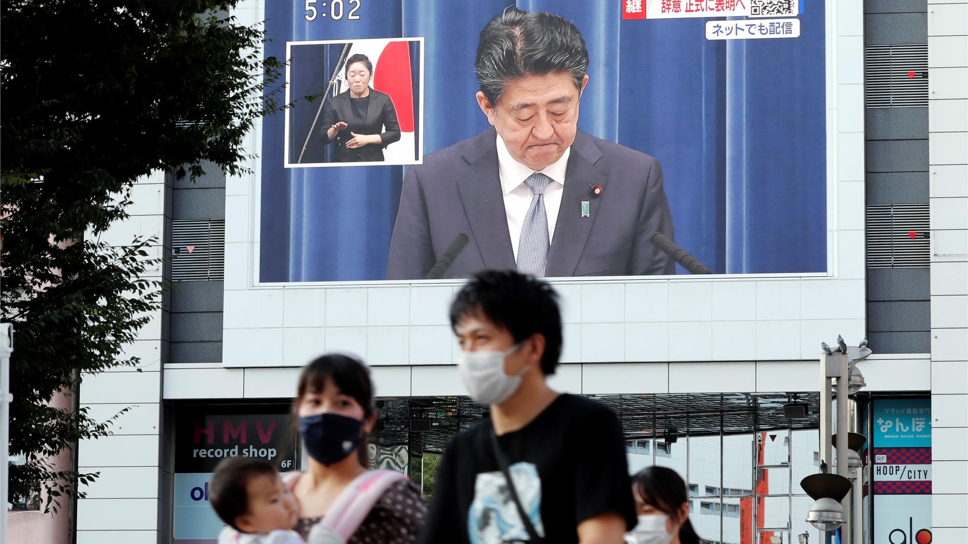 People walk past a large screen in Tokyo, Japan, broadcasting the news conference of Japanese Prime Minister Shinzo Abe where he announced his resignation. 
