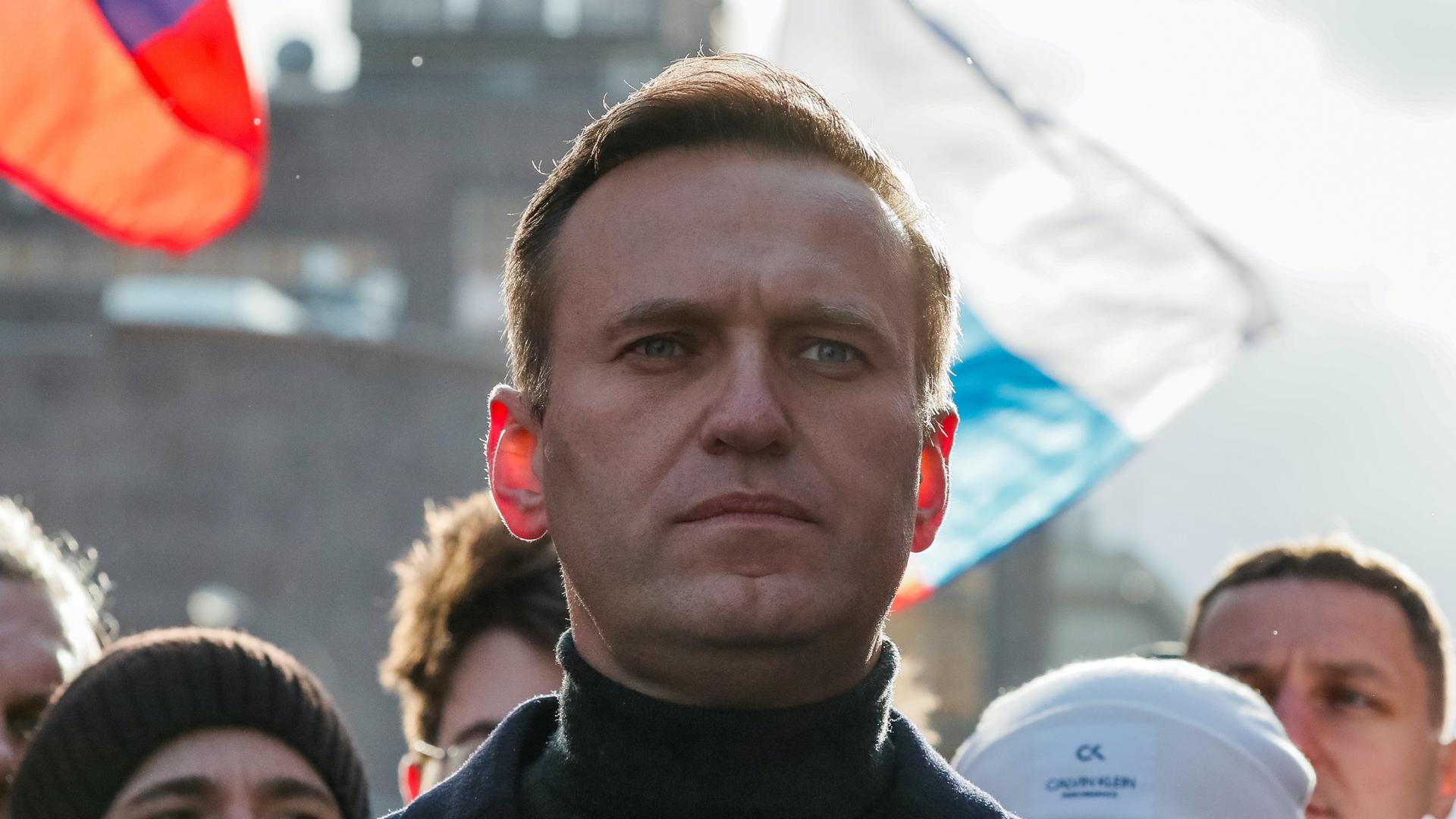 Close up of Alexei Navalny, a white man with short hair wearing a turtle neck and a few people standing behind him