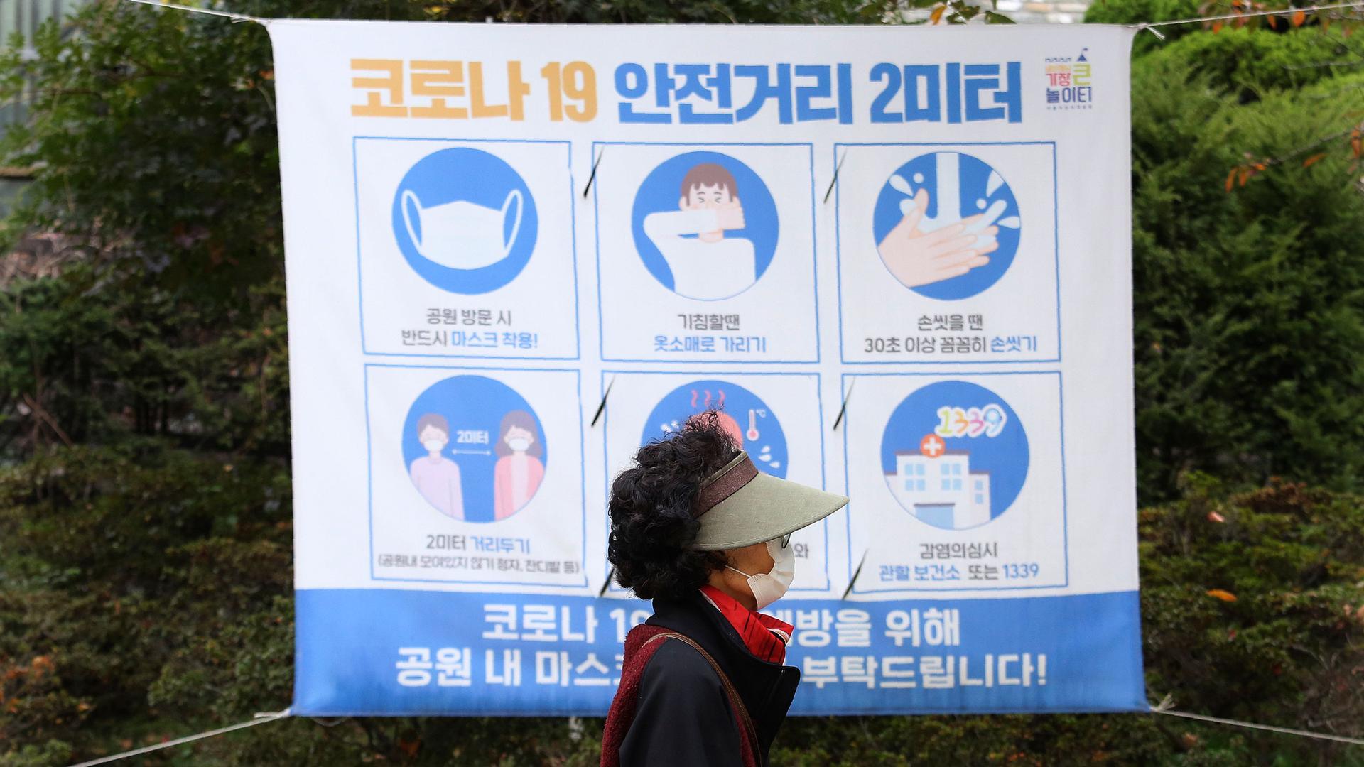 A woman is shown wearing a visor and face mask while walking past a poster with guidance on stopping the spread of the coronavirus.