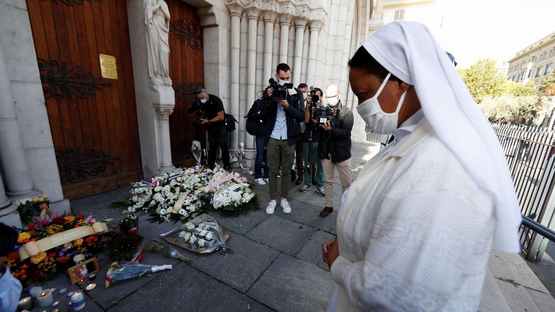 A nun prays in front of candles and flowers left in tribute to the victims of a deadly knife attack at the Notre Dame church in Nice, France, Oct. 30, 2020.