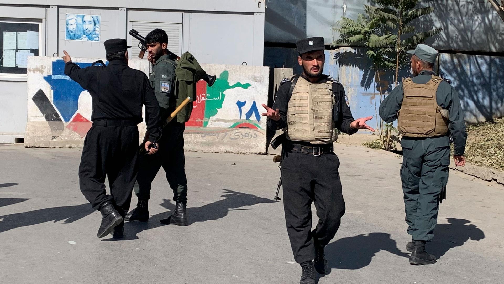 Several Afghan security officials are show wearing body armor and holding weapons.