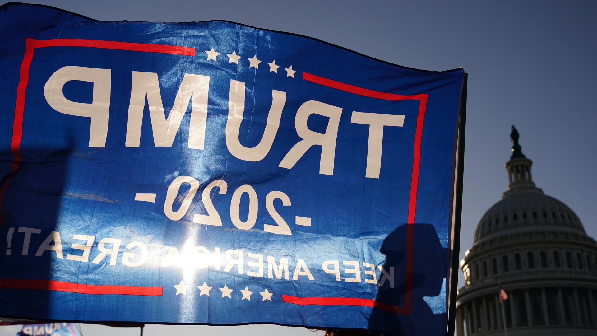 A supporter of President Donald Trump holds a Trump 2020 flag with sun shining through it outside the US Capitol building as they attend pro-Trump marches