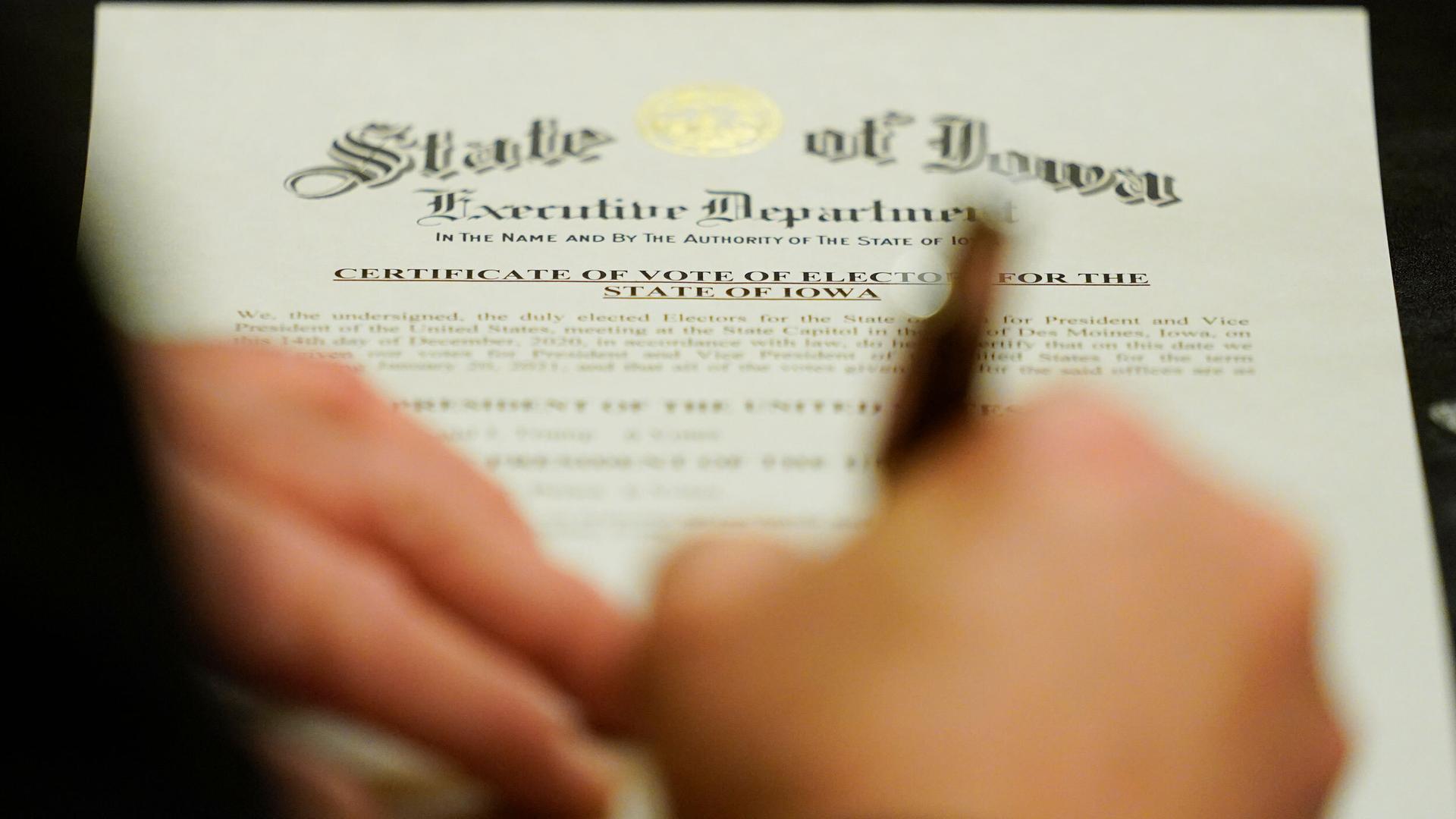 A member of Iowa's Electoral College signs the Certificate of Vote of Electors for the State of Iowa at the Statehouse in Des Moines, Iowa, Dec. 14, 2020.