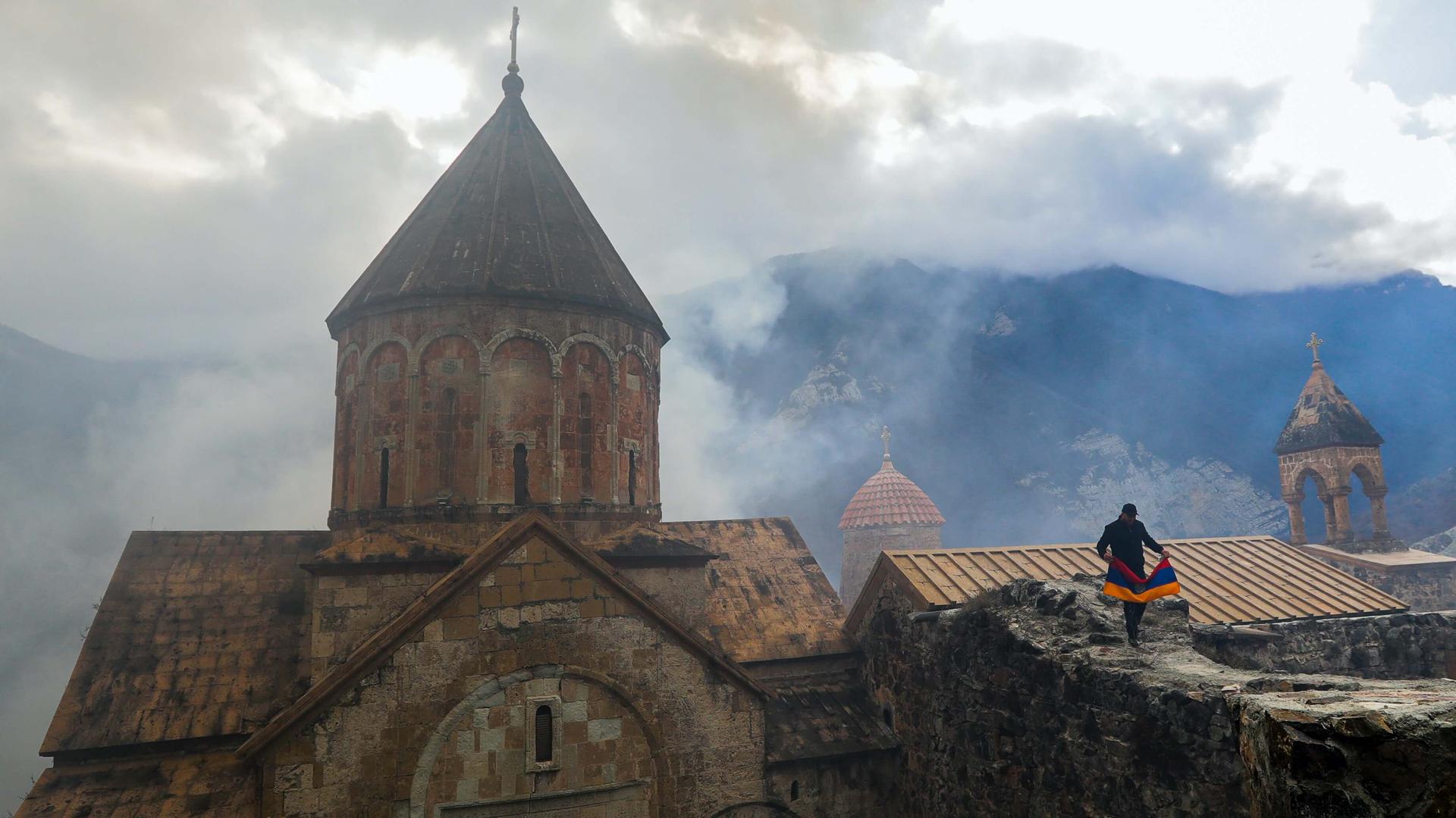 A man with an Armenian national flag visits a 12th-13th an old brick monastery surrounded by mountain vistas