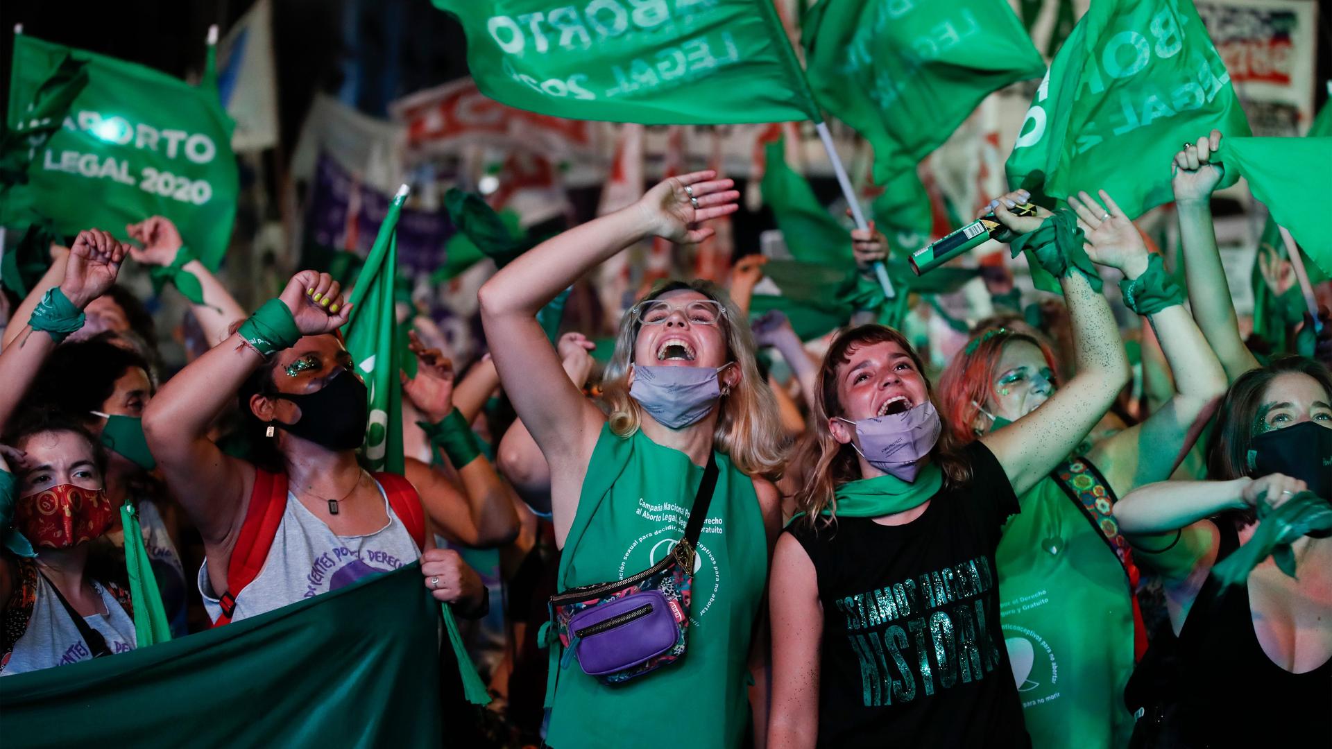 A group of women raise their arms and wave green flags