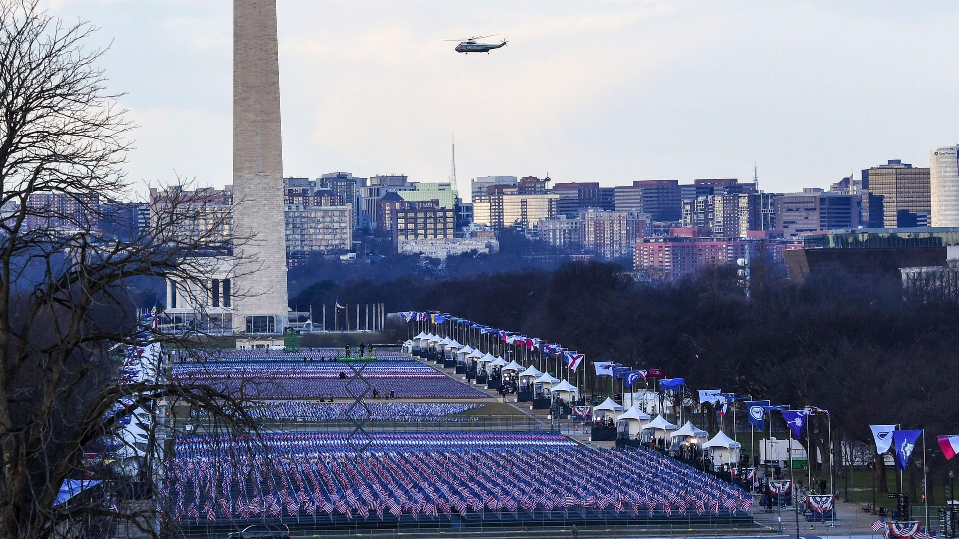 The US National Mall is shown covered in flags with the Washington Monument in the distance and the Marine One helicopter flying past.