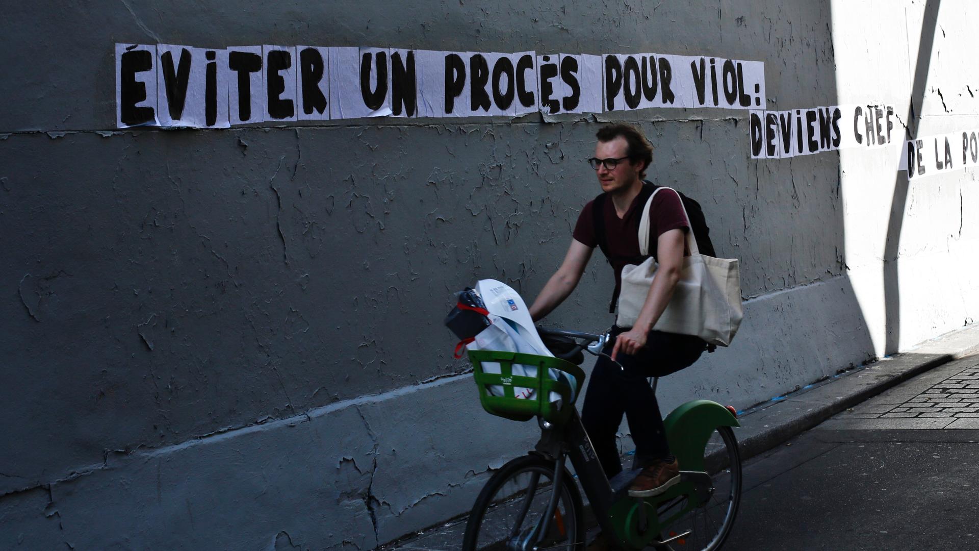 A man rides a bike by a slogan pasted on a wall reading 