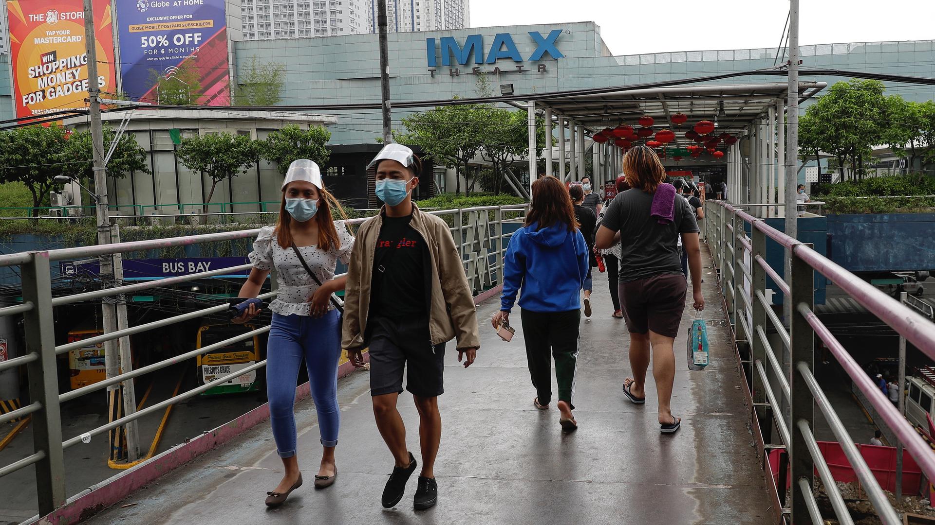 People walk wearing face masks and shields over a bridge near a mall